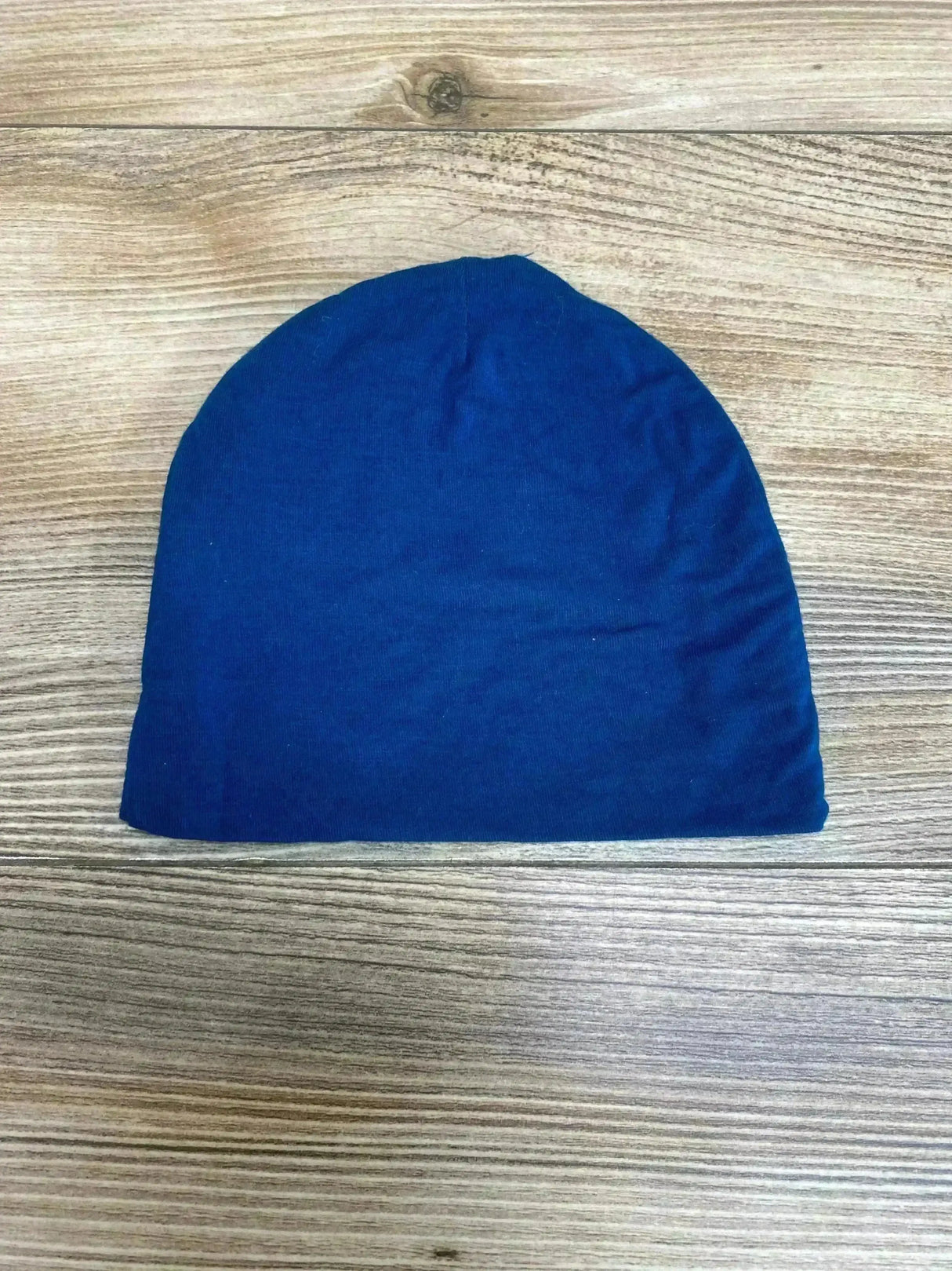 Flat lay of Posh P baby beanie showing solid blue soft stretch knit and rounded crown on light wood background