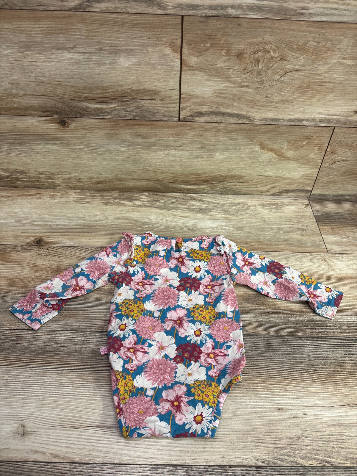 Ruffle Butts blue long sleeve floral bodysuit for babies laid on a wood floor