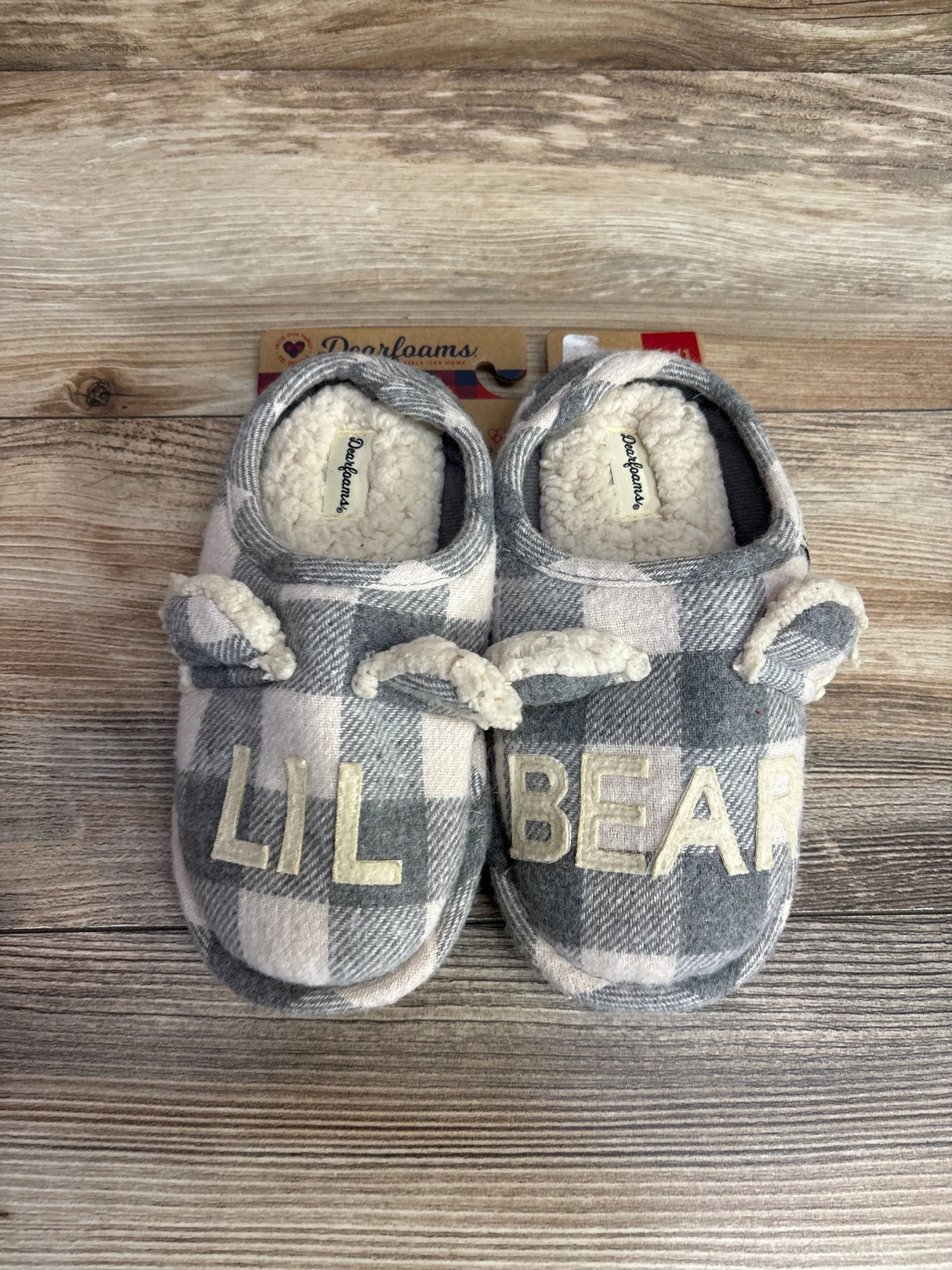 Children's plaid slippers with cream sherpa lining and "LIL BEAR" text on top, set on wooden surface