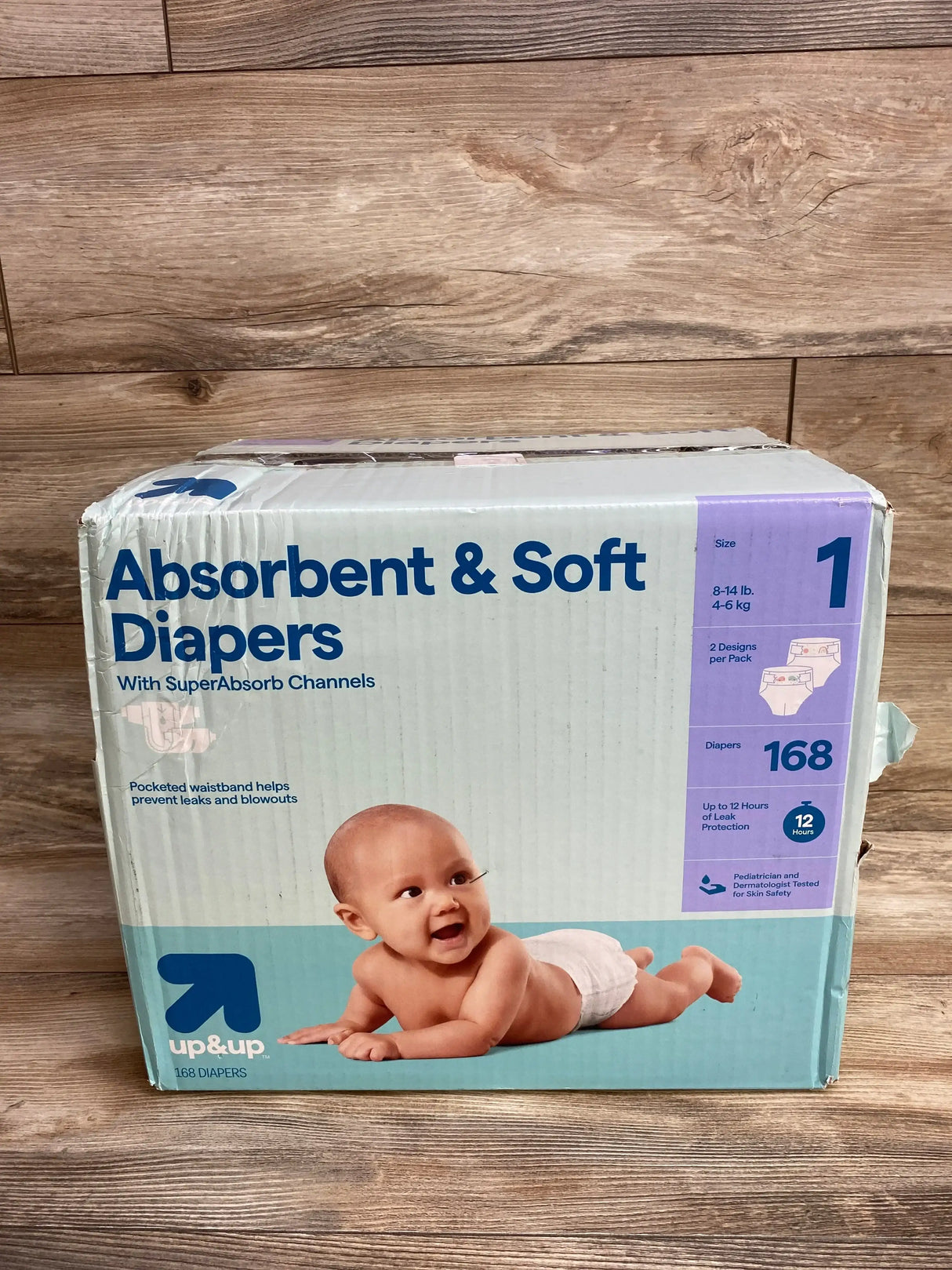 Box of size 1 up&up baby diapers with smiling baby, 168 count, on wood background