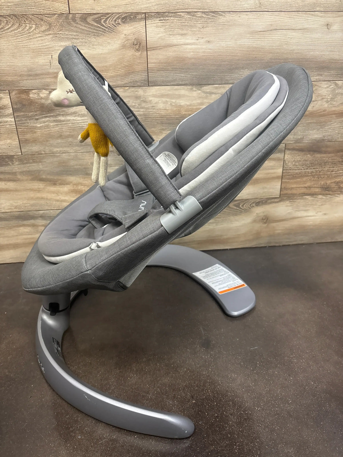 Side view of Nuna Leaf Grow baby swing showing curved base and toy bar with hanging plush against wood background