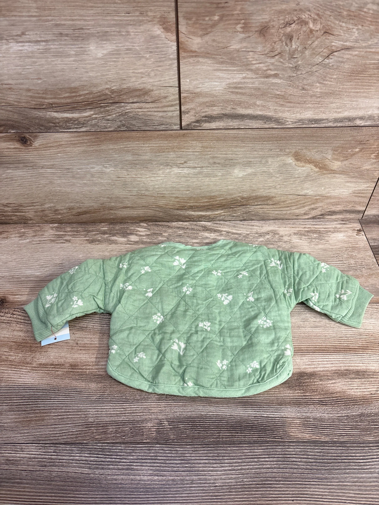 Green quilted baby jacket with white floral print on wooden background