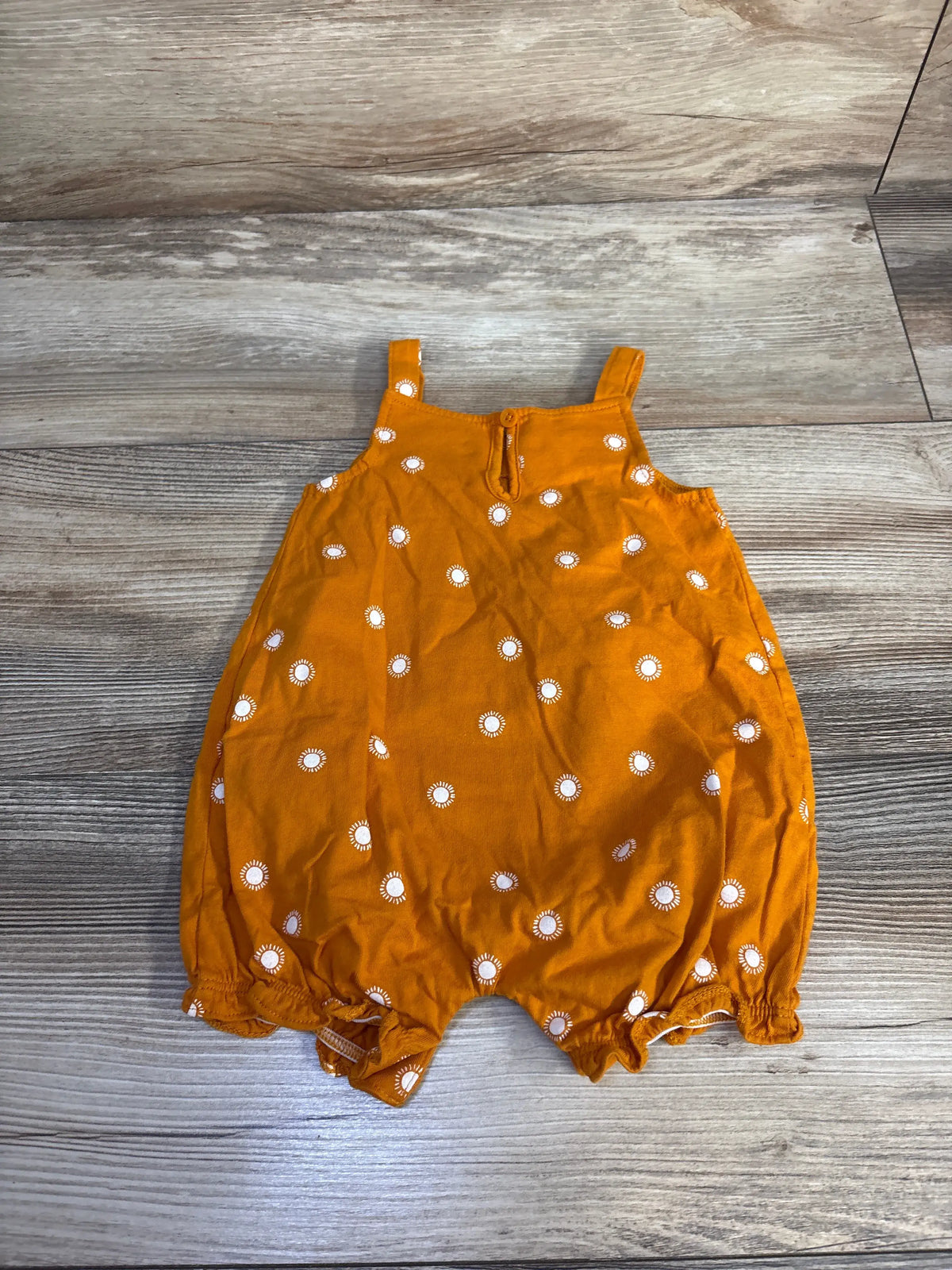 Front view of Carter’s Sun Shortie Romper in orange showcasing white sunburst pattern and elastic leg openings on a wood grain floor
