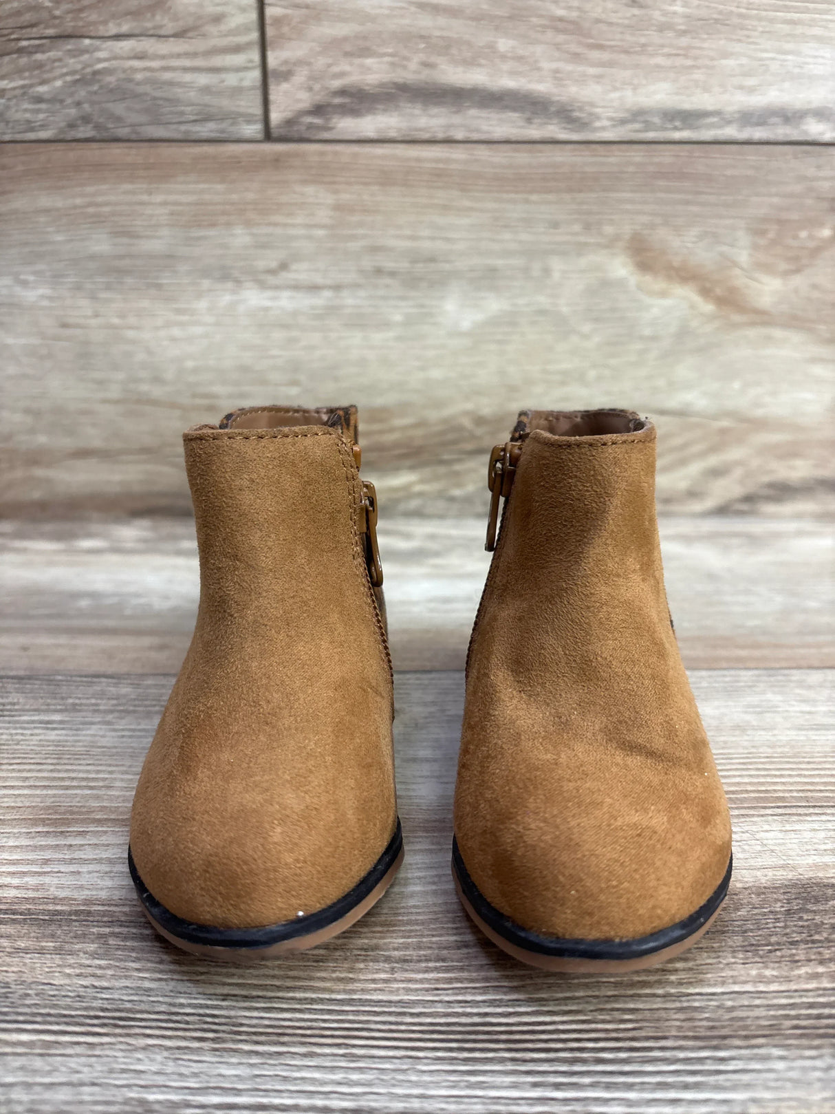 Pair of toddler brown suede ankle boots with side zippers on wooden floor