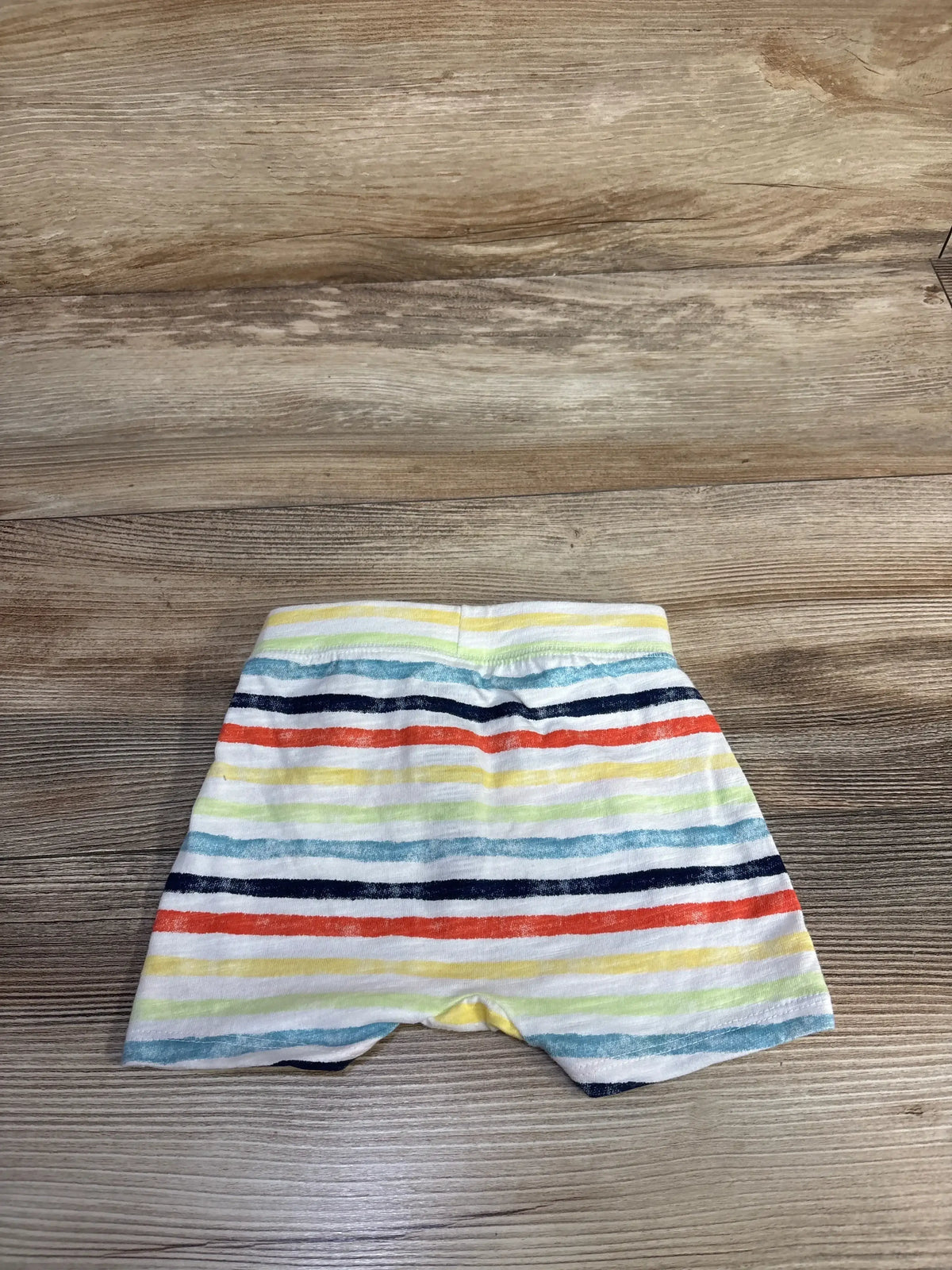 Back view of Jumping Beans baby shorts showcasing multicolored horizontal stripes and elastic waistband on wood surface