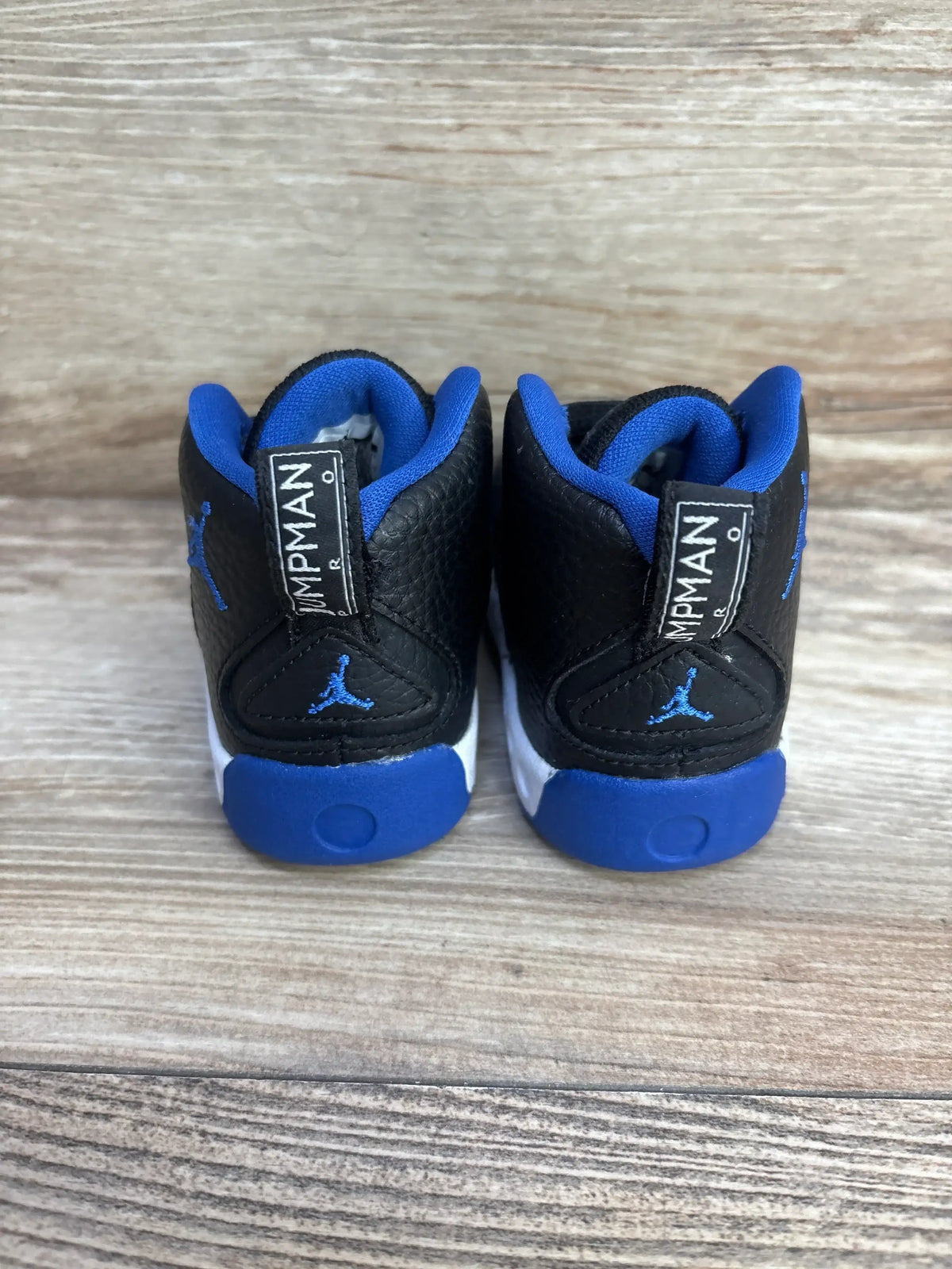 Back view of Air Jordan Jumpman Pro BT Sneakers showcasing black heel with royal blue trim and Jumpman pull tabs on wood plank floor