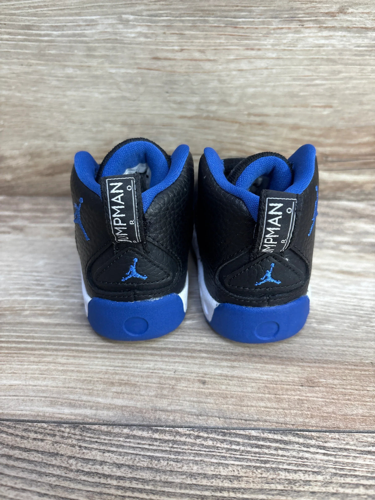 Rear view of Air Jordan Jumpman Pro BT toddler sneakers showing black pebbled leather and blue lining with wood background, size 5C