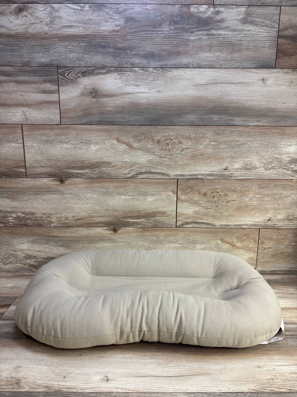 Beige oval pet bed on wood floor background, cozy dog or cat bed