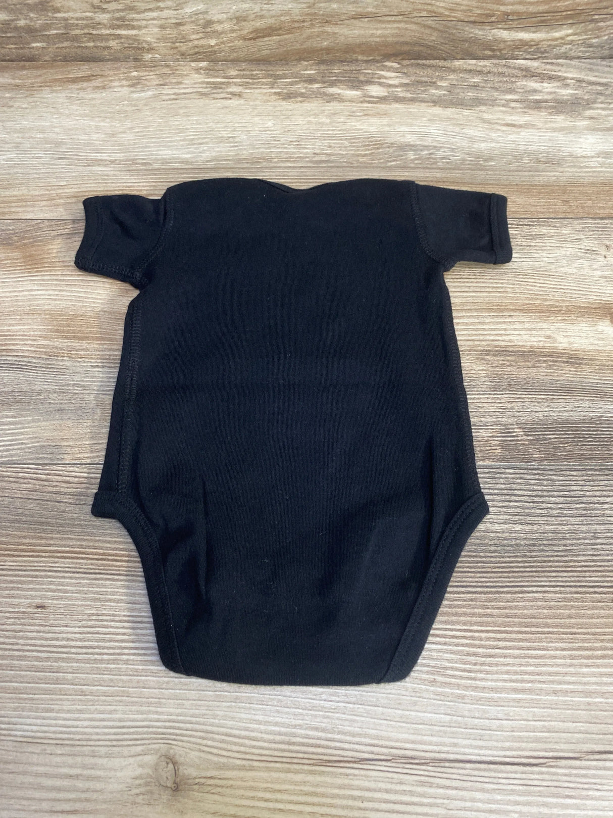 Top-down view of black Rabbit Skins short-sleeve baby bodysuit, size 3–6 months, laid flat showing solid color and crew neckline on wood background
