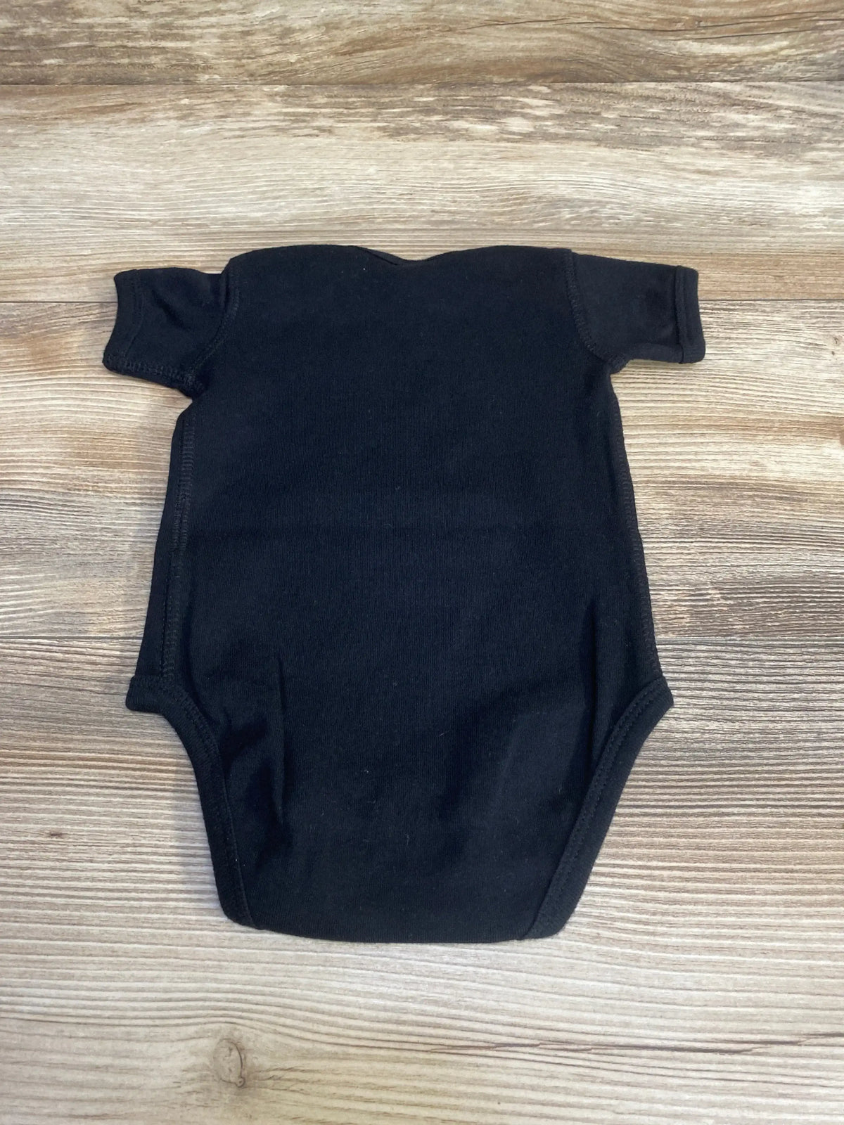 Back view of black Rabbit Skins bodysuit in size 6M showing short sleeves and plain cotton fabric on a wood-grain background