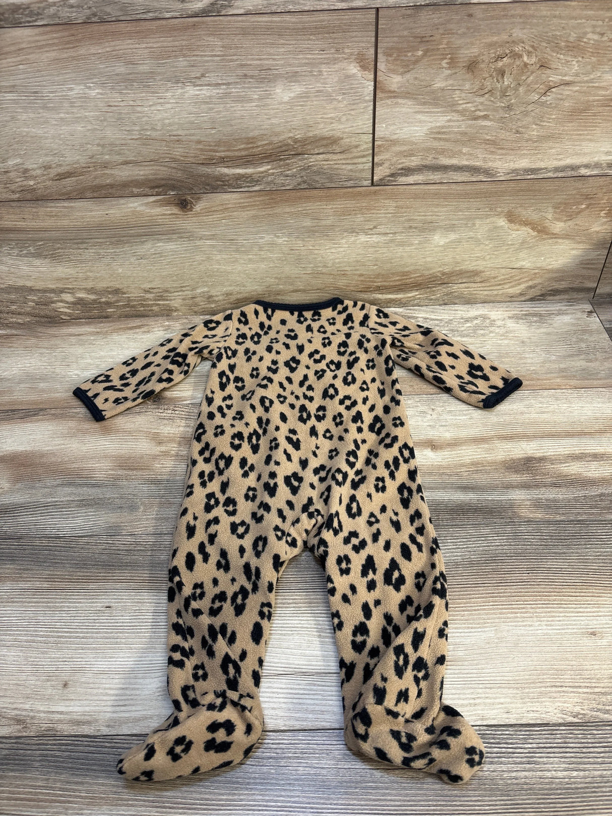 Leopard print baby footed sleeper with long sleeves on wooden floor