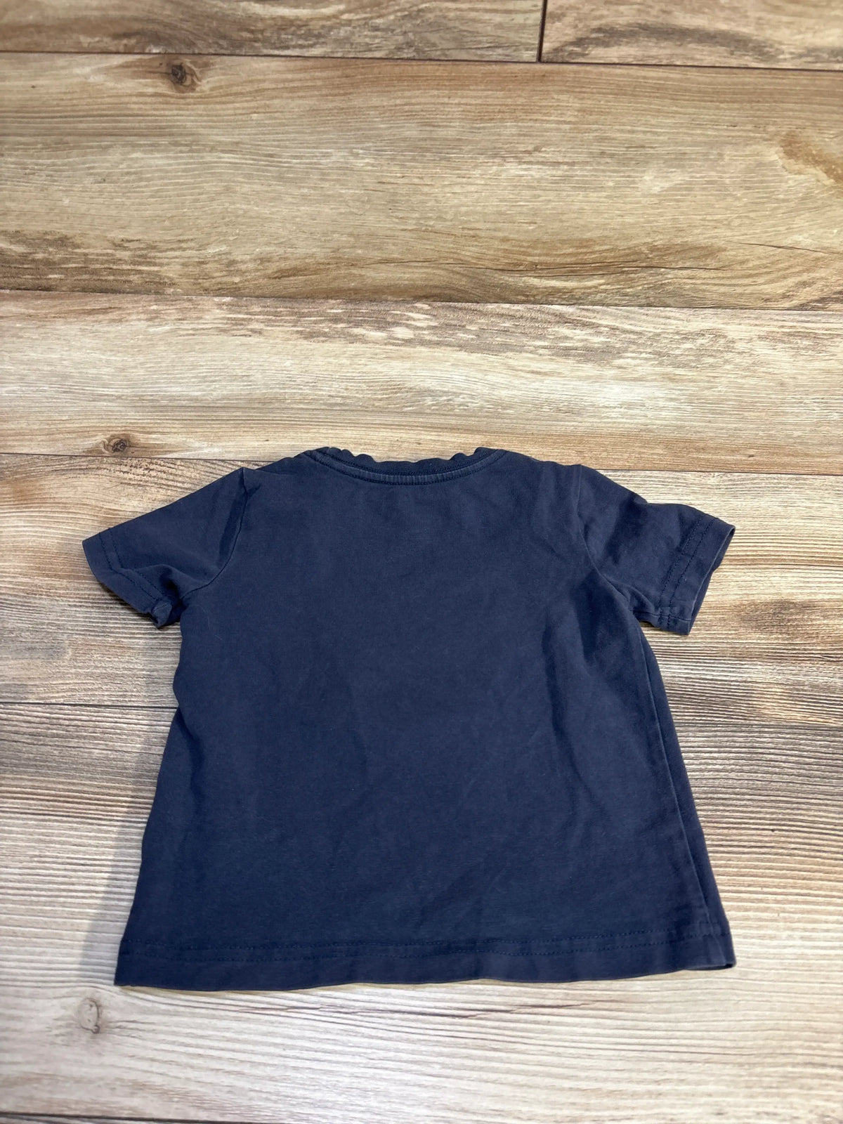 Front view of Tommy Bahama navy short sleeve shirt in size 12 months laid flat on a wood-grain background