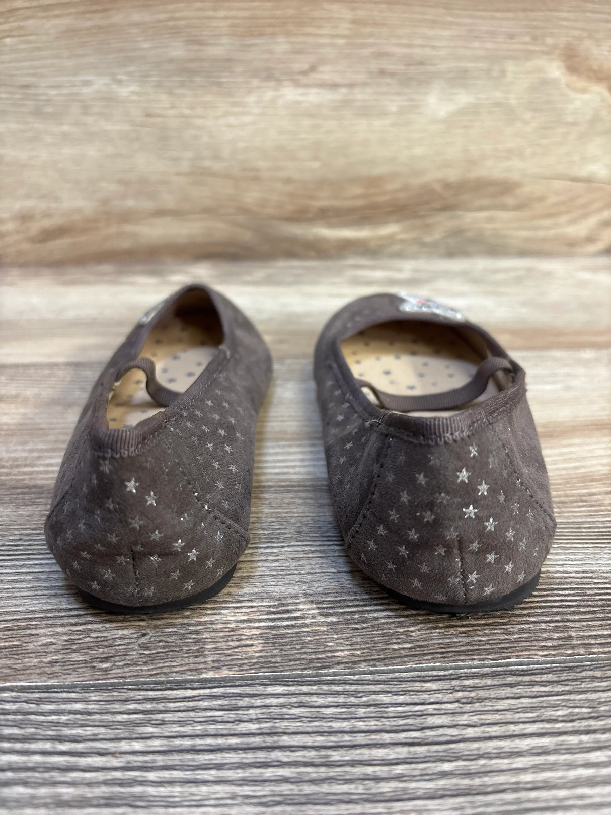 Rear view of Cat & Jack star applique toddler flats in brown showing silver star pattern and elastic strap on wooden floor