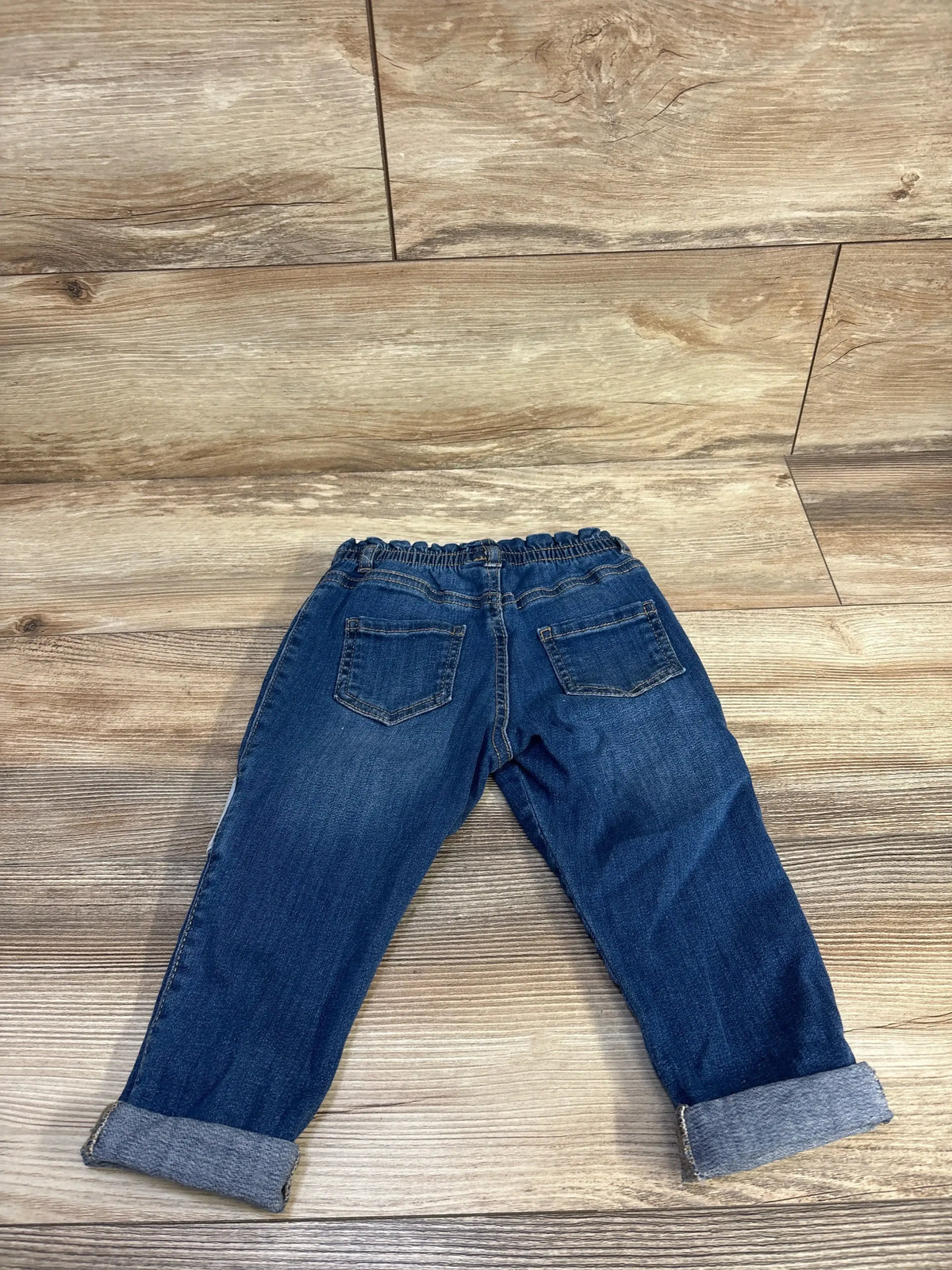 Back view of Mayoral newborn blue jeggings showcasing elasticated waistband, back pockets, and rolled cuffs on a wood floor