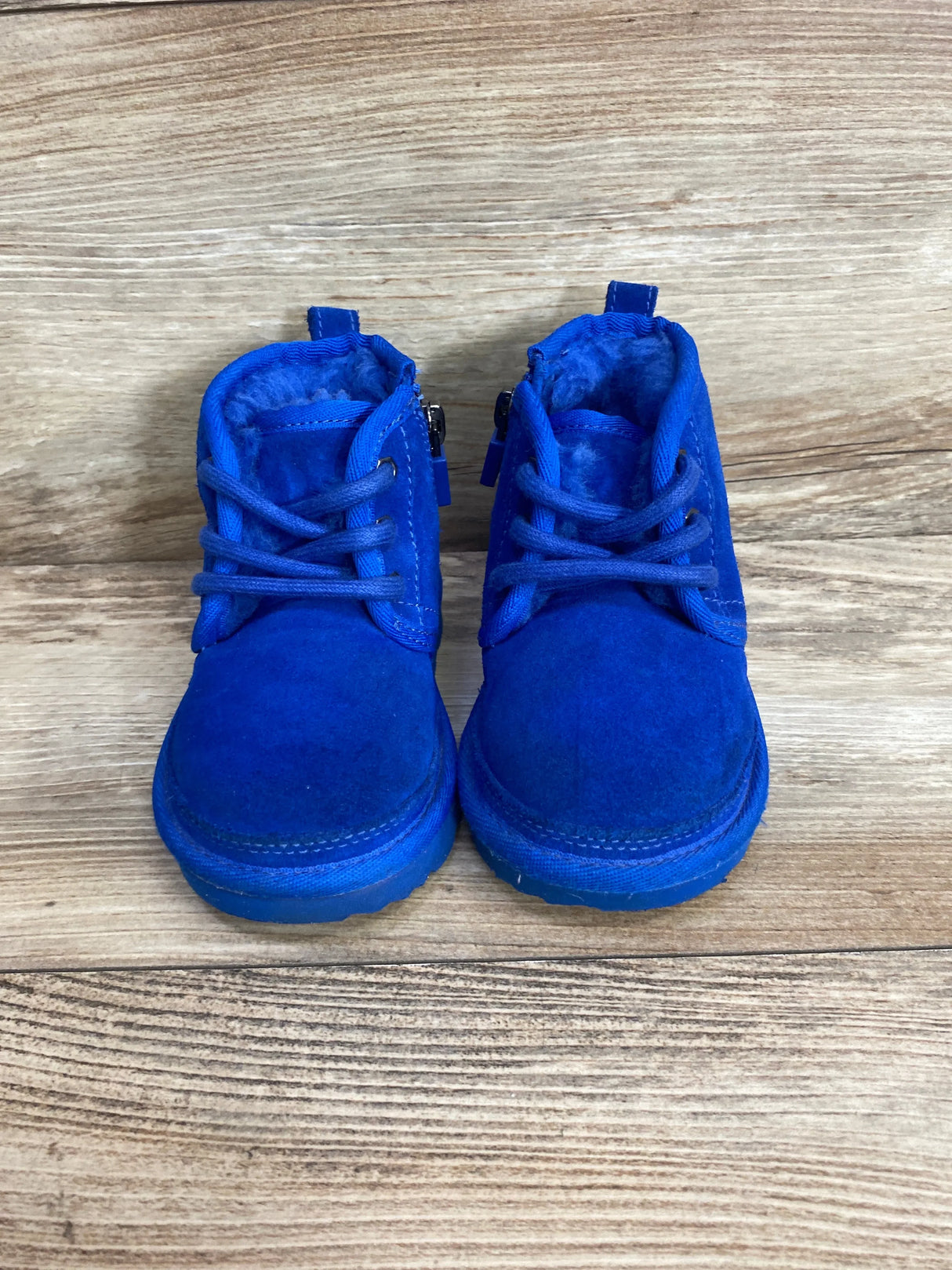 Front view of pair of bright blue suede toddler boots showcasing laces side zippers and fleece lining on wood plank floor