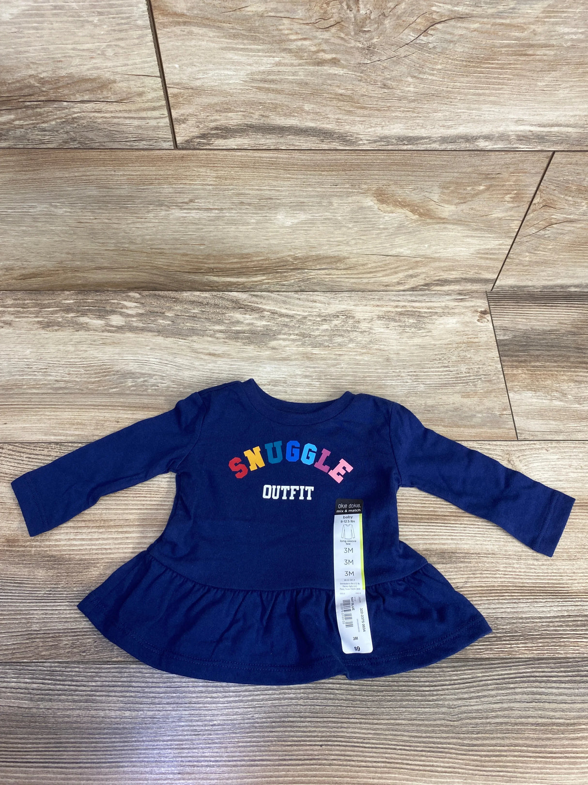 Navy blue long sleeve baby dress with colorful SNUGGLE OUTFIT text, size 3 months, on wood floor