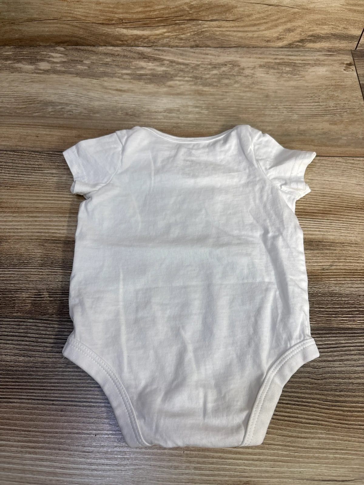 Flat lay of Adidas white baby bodysuit showcasing short sleeves and cotton fabric on a wood surface