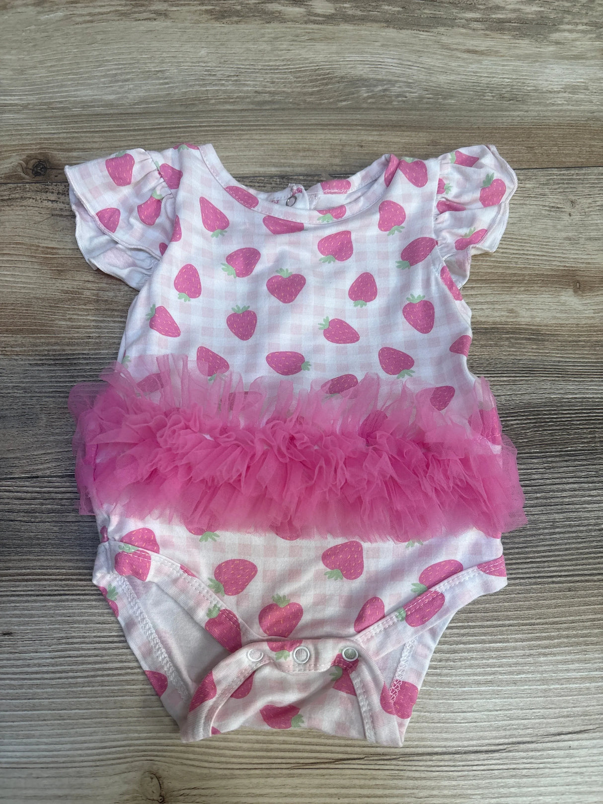 Pink strawberry print baby girl bodysuit with ruffled tutu on wood background