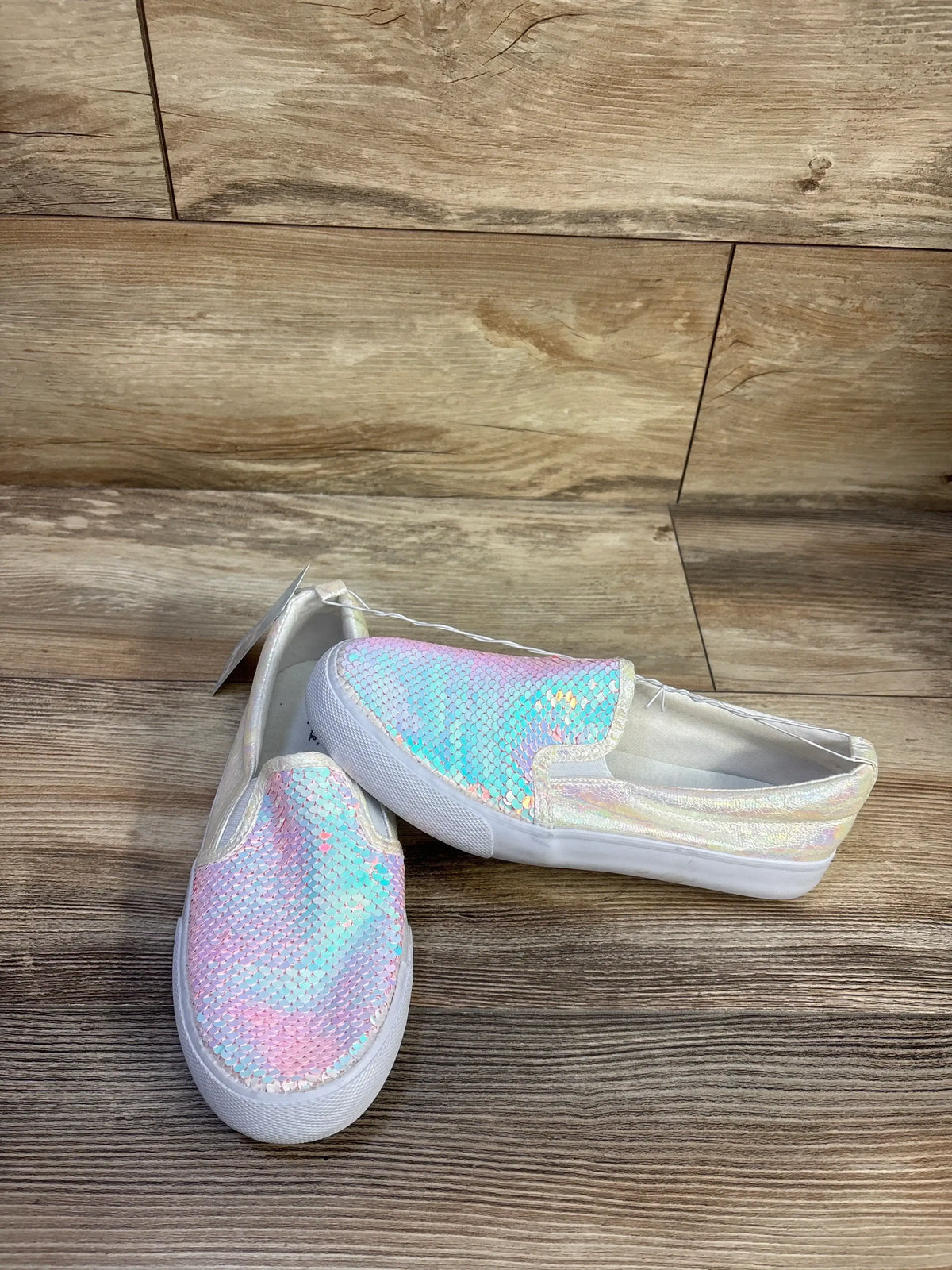 Side and front view of Cat & Jack Aliki slip-on sneakers with iridescent pastel sequins and white soles on wood background