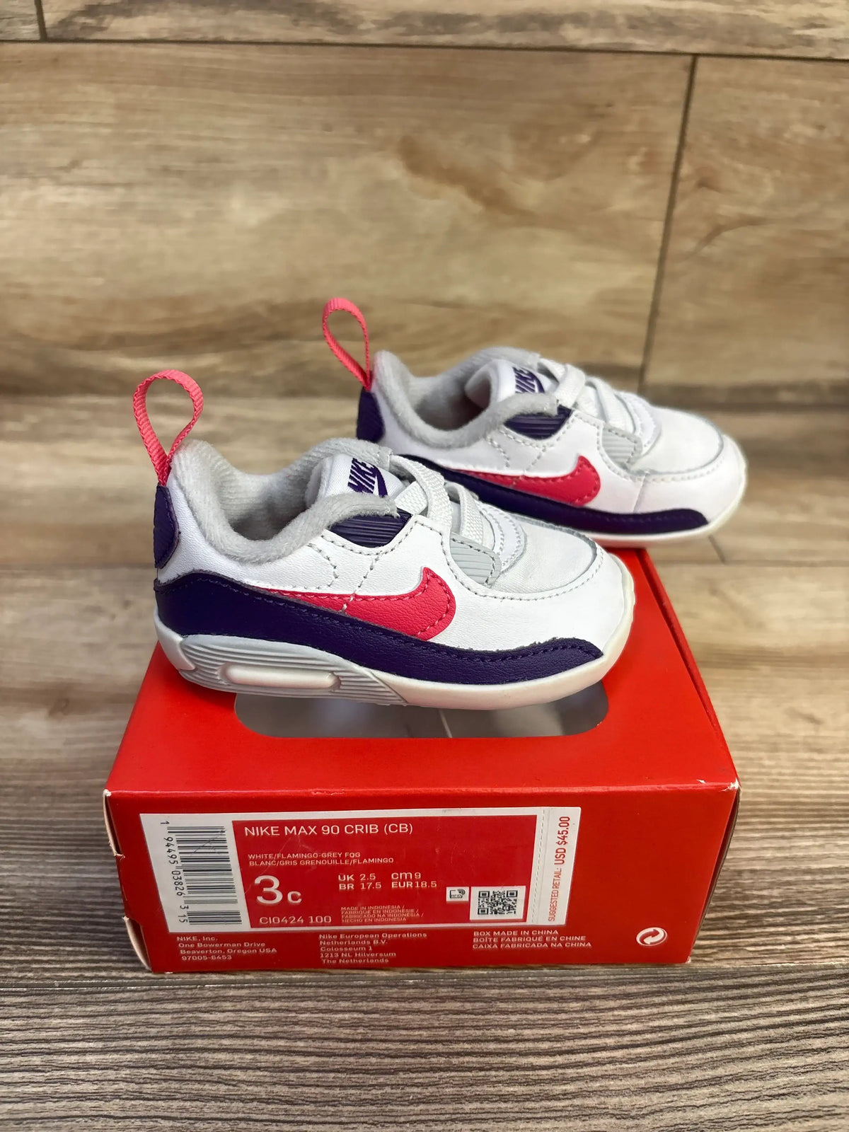 Side view of Nike Air Max 90 Crib sneakers size 3C showcasing white upper with pink Flamingo Swoosh and purple trim on red Nike box