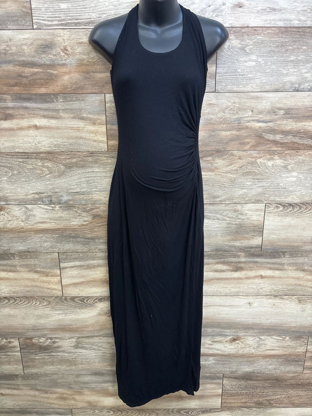 Front view of black maternity tank maxi dress showing side ruching over the belly on a mannequin against a wood plank background