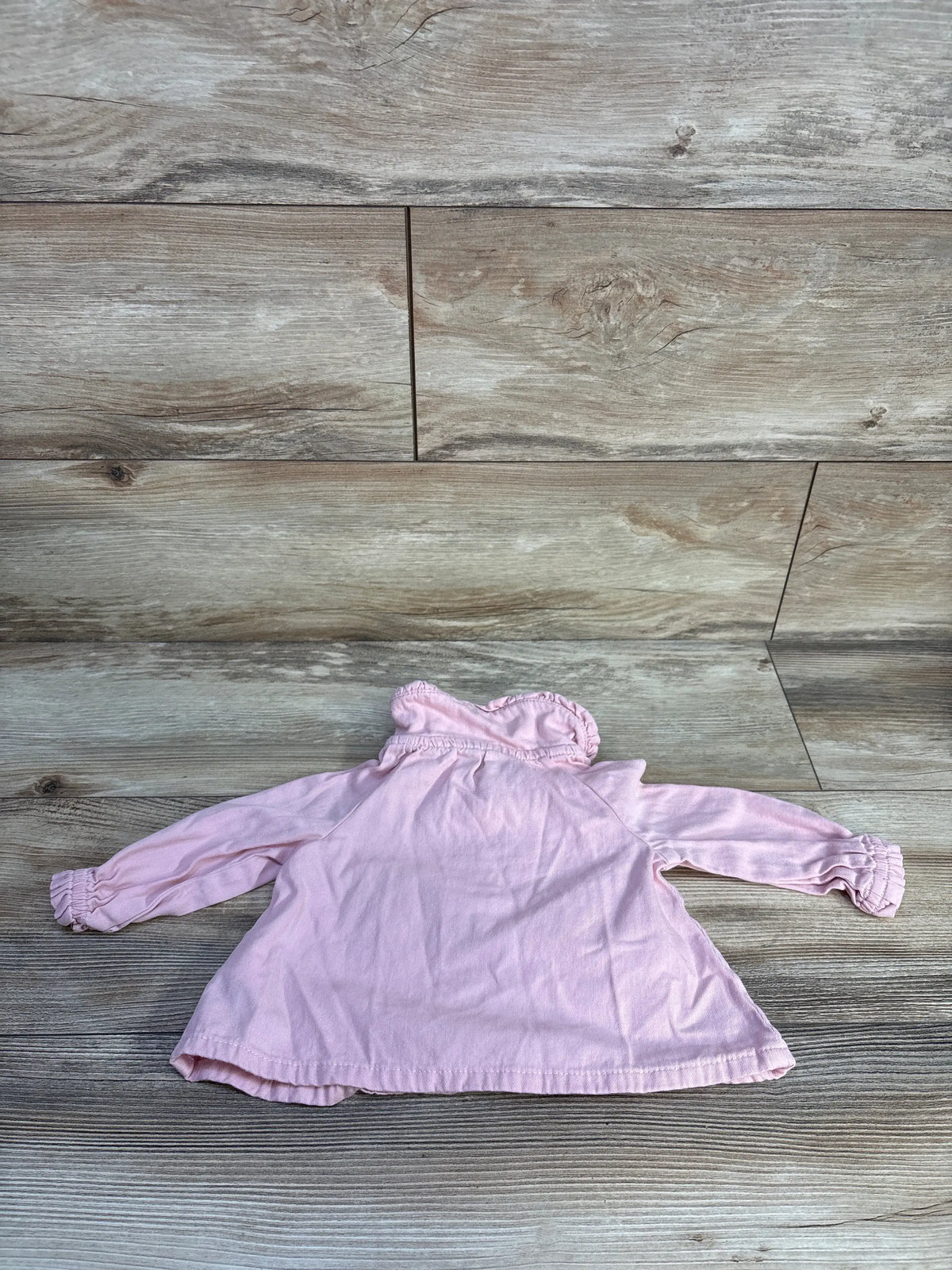 Front view of Baby Gap pink denim henley top showcasing long sleeves and ruffled cuffs on a wood grain floor