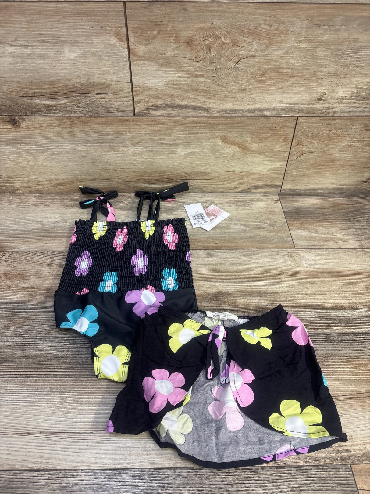 Top-down view of Jessica Simpson black smocked swimsuit and matching floral skirt set on a wood floor