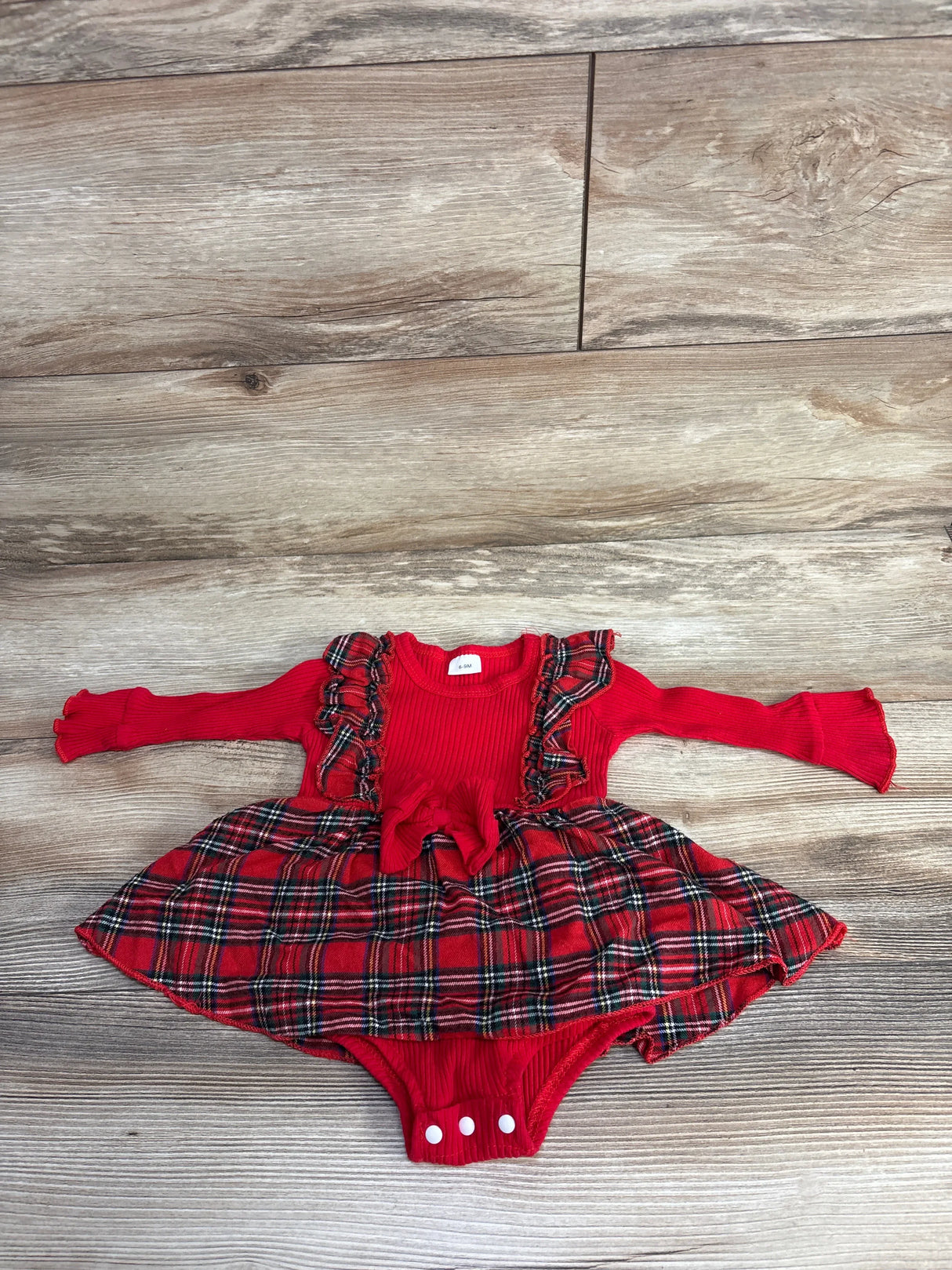 Red plaid baby dress with ruffle details and long sleeves, laid on wood floor