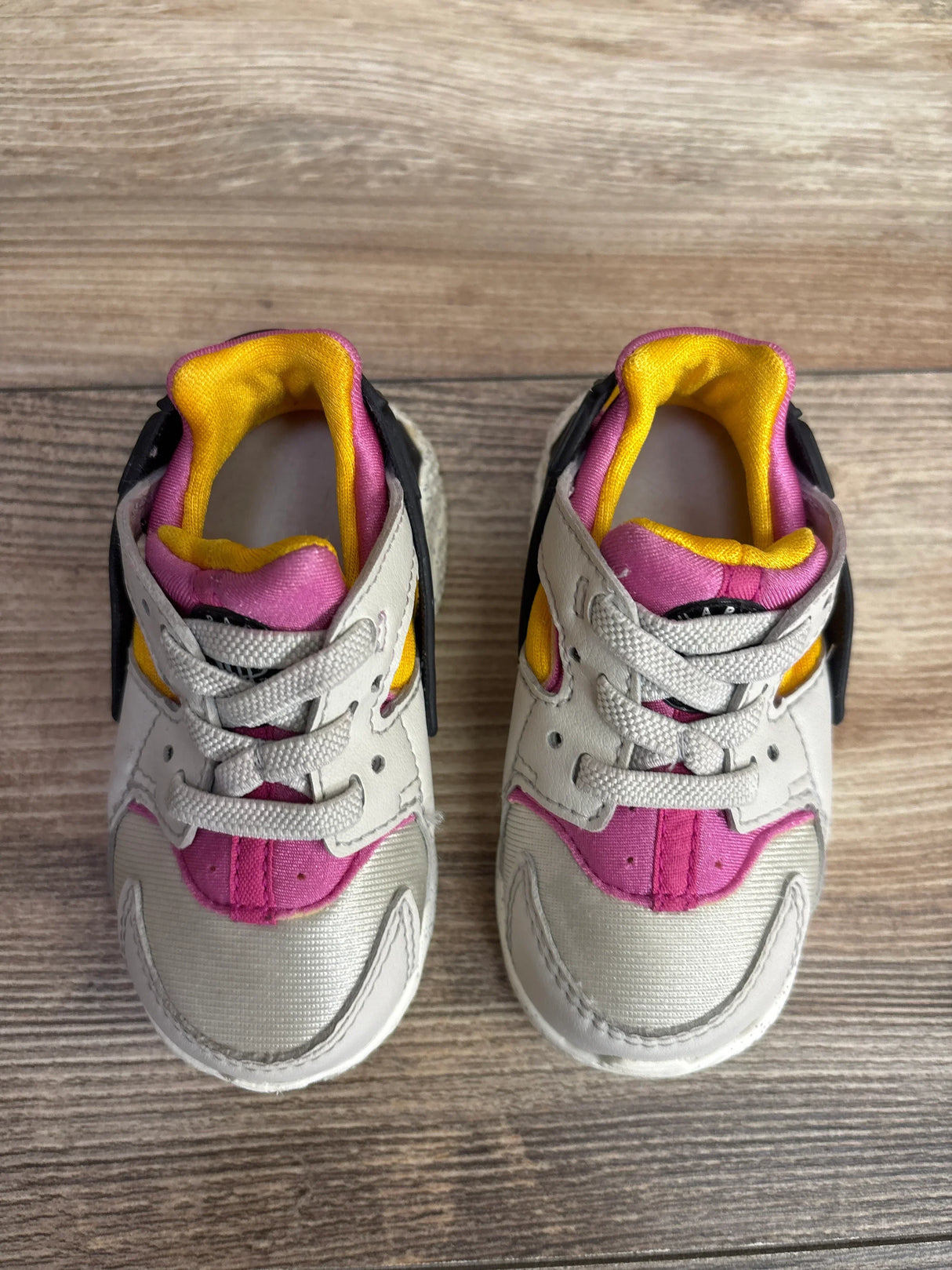 Pair of toddler sneakers with pink, yellow, and gray accents on wooden floor