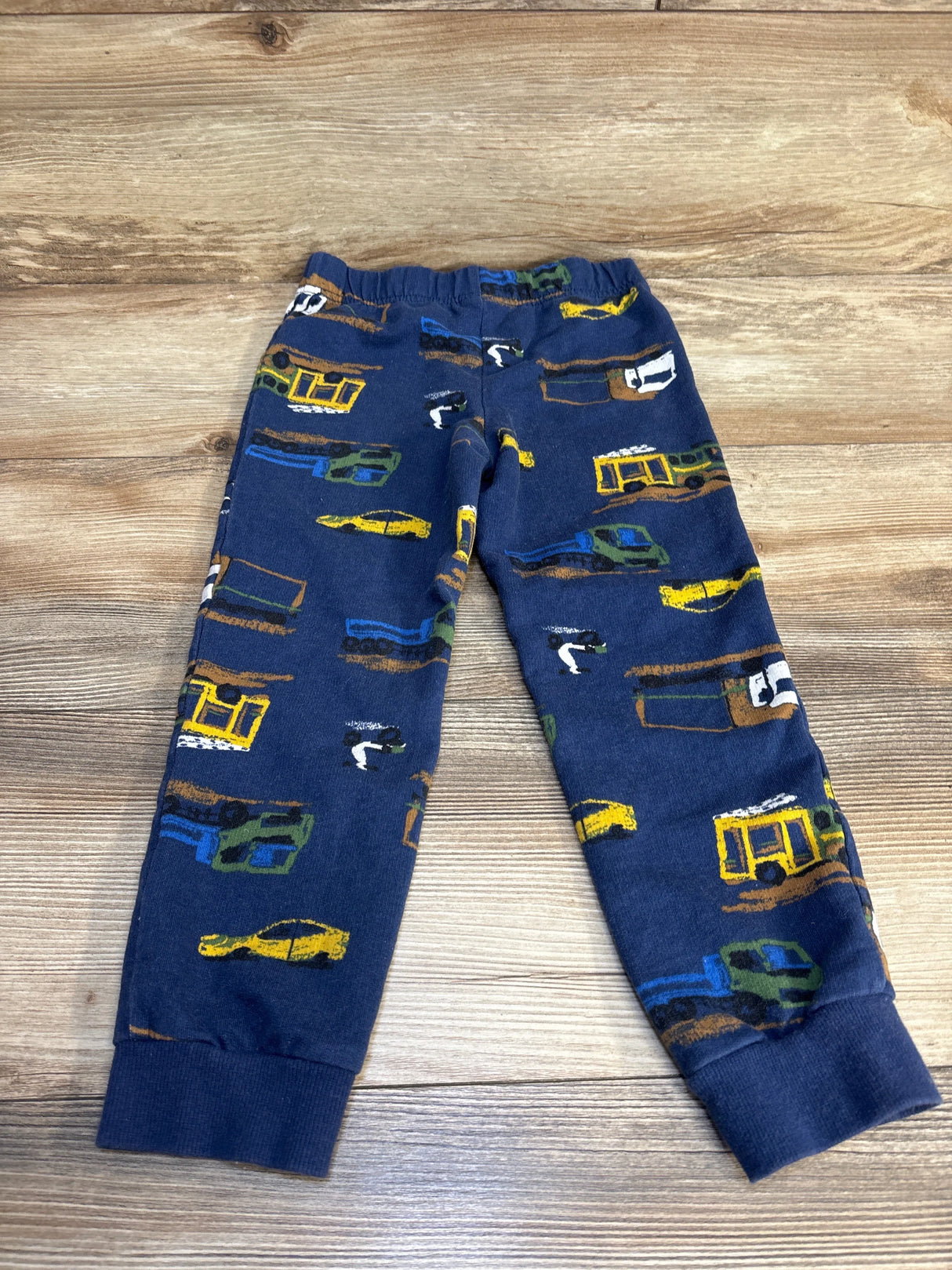 Blue kids pants with colorful construction vehicle print, laid on wood floor