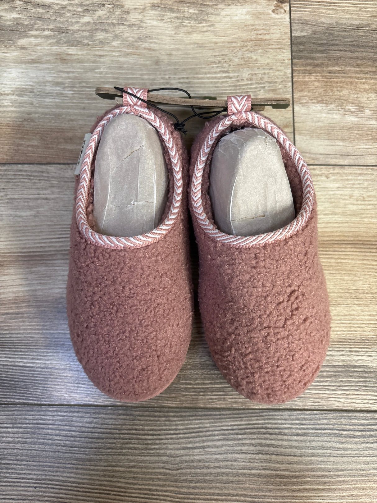 Top down view of pink Pawz Cozy toddler slippers showcasing plush sherpa texture and striped trim on wood floor background