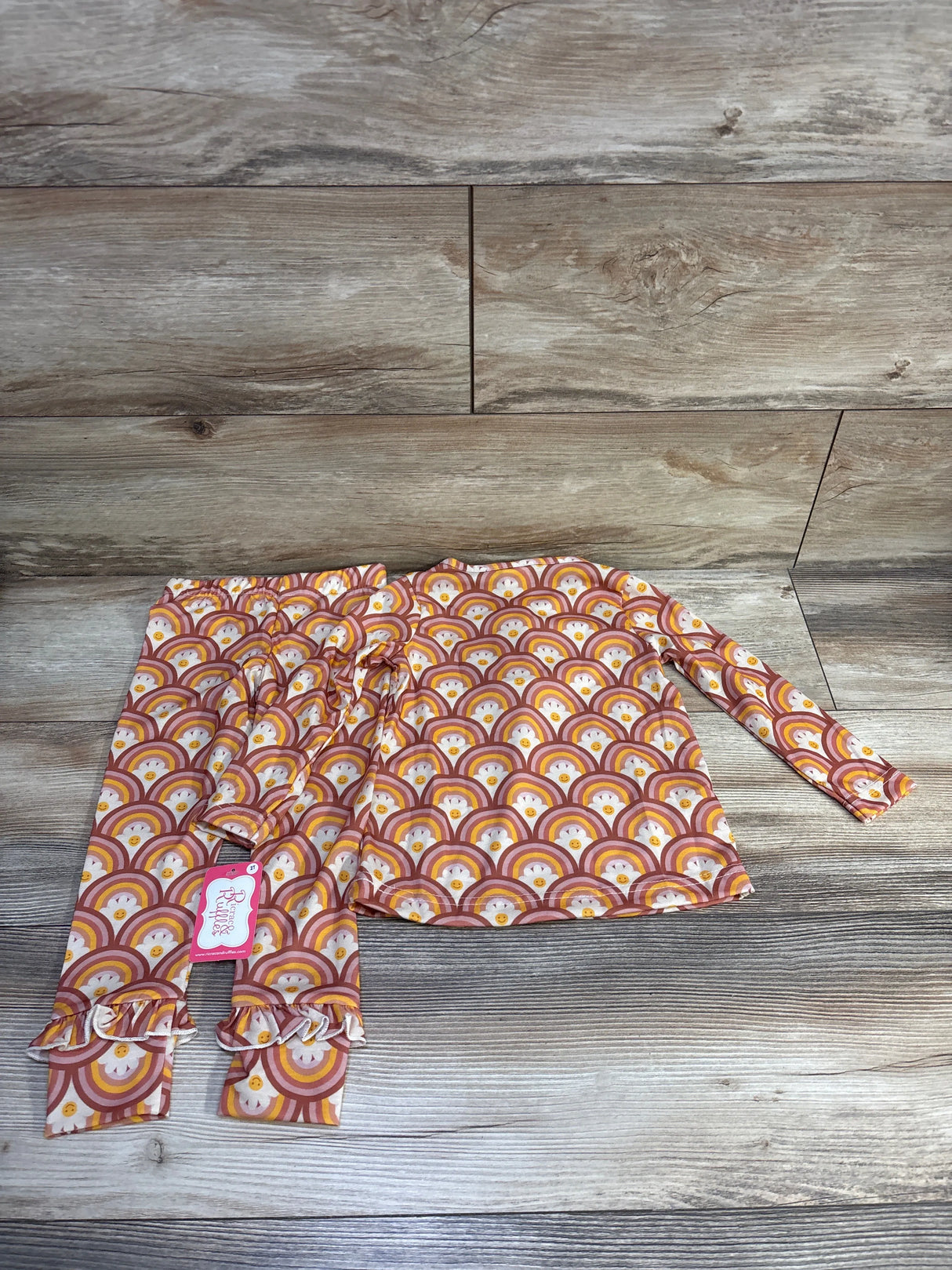 Flat lay of toddler 2-piece shirt and pants set in size 2T showcasing orange rainbow print, ricrac trim and ruffled cuffs on wood background