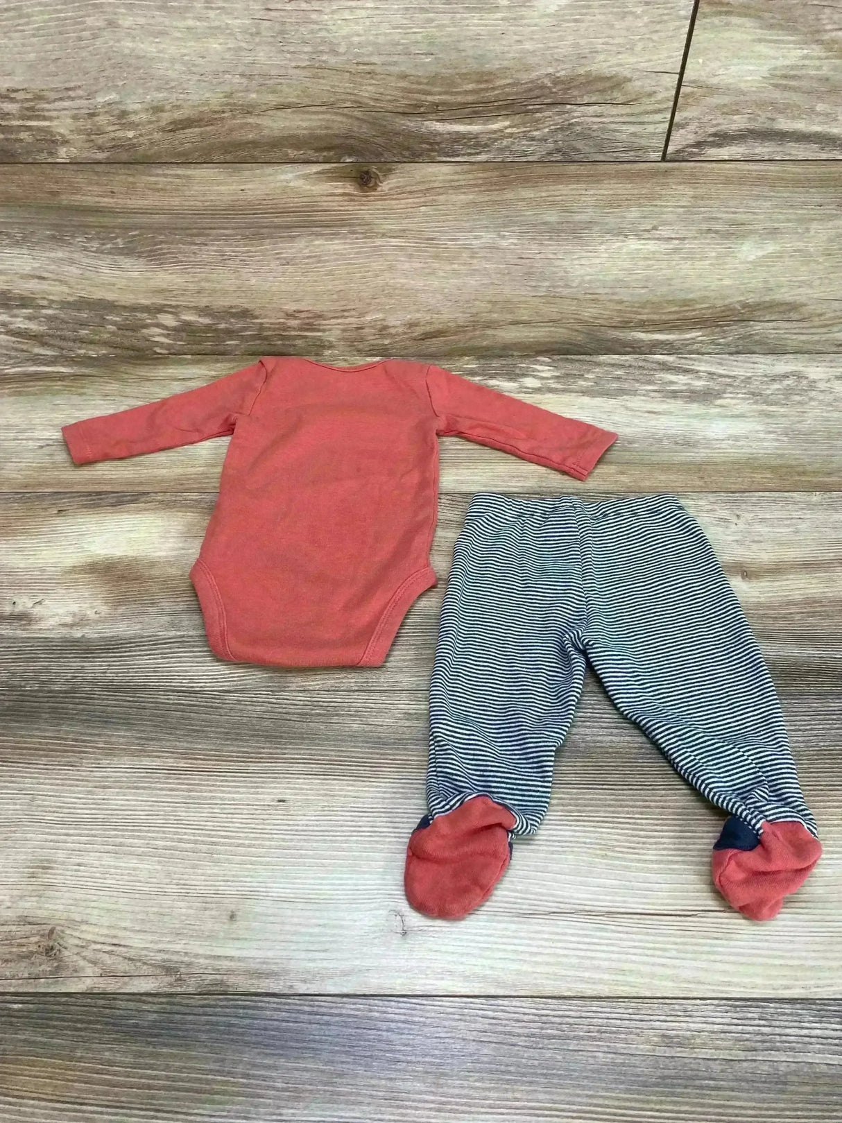 Flat-lay of Carter's 2-piece baby bodysuit set: coral long-sleeve bodysuit and navy-striped footed pants on wood background