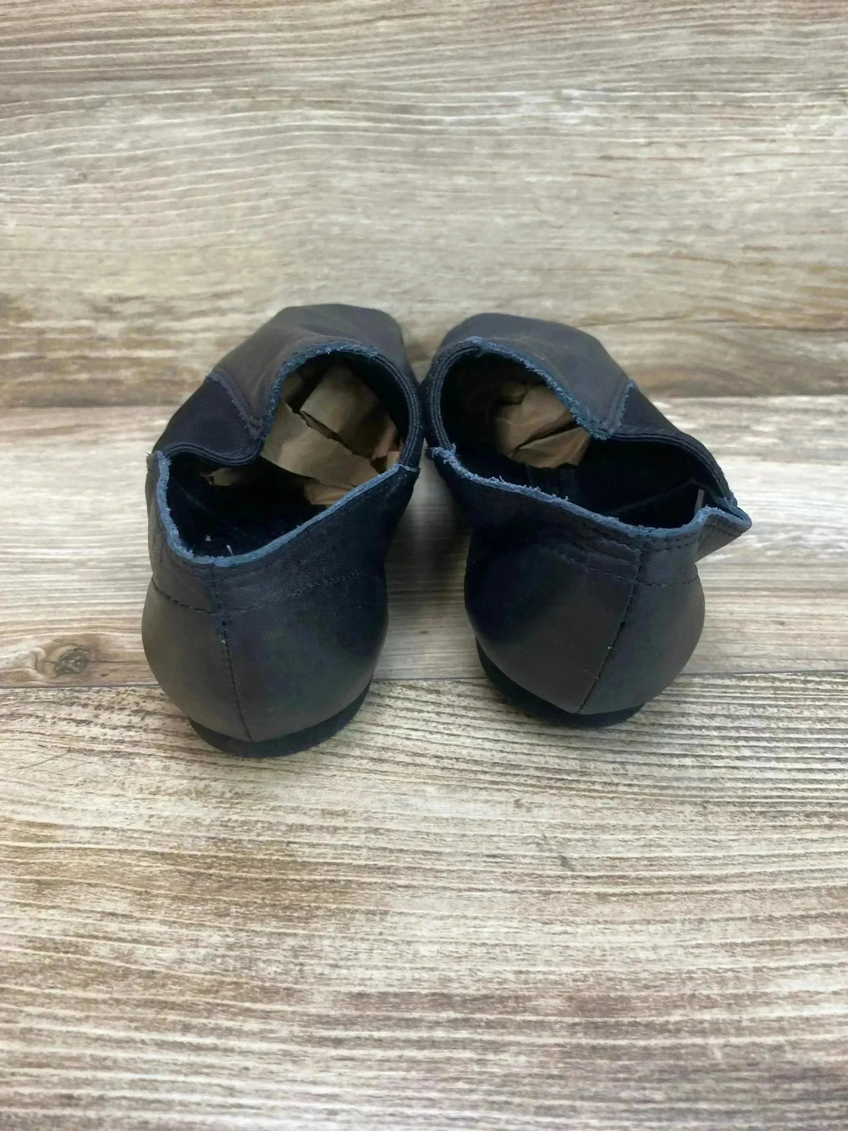 Rear view of Capezio E-Series black jazz slip-on shoes, size 8C, showing frayed heel collars and paper stuffing on wood background