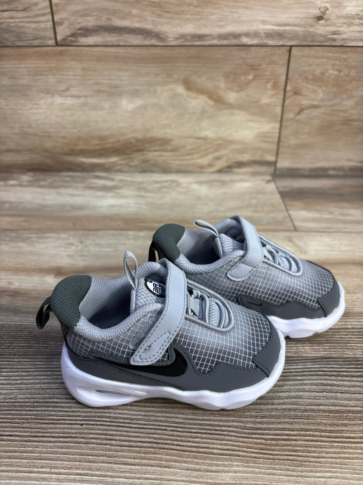 Three-quarter view of Nike Air Max Nova TD toddler sneakers in Wolf Grey with hook and loop closures on wood-look flooring