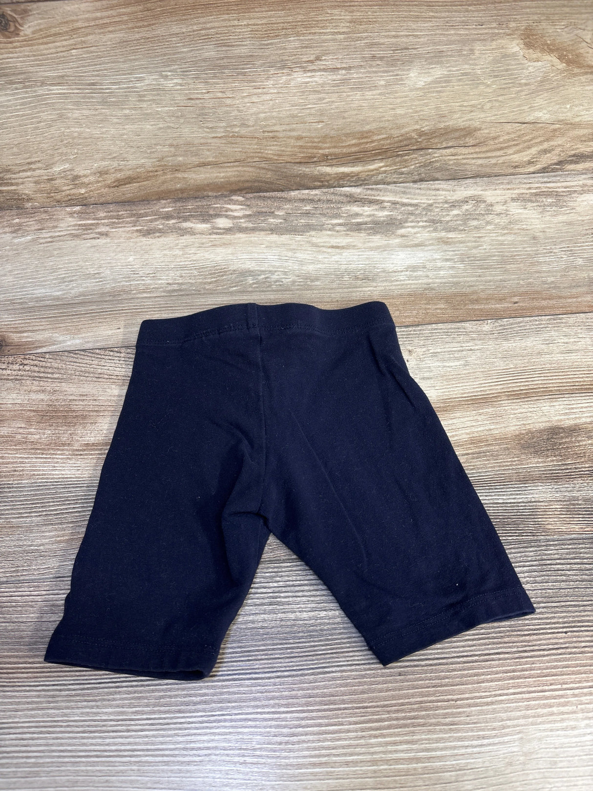 Top-down view of navy H&M toddler bike shorts (size 4T) showing elastic waistband and mid-thigh length on wood floor