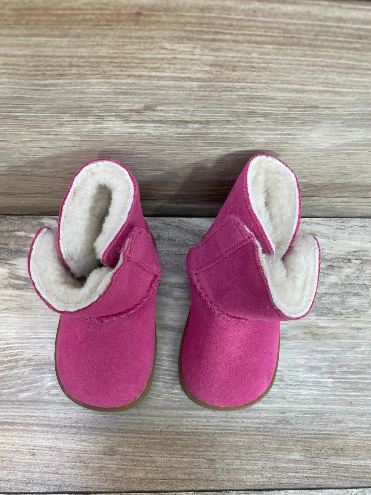 Top view of UGG Keelan toddler boots showcasing pink suede and folded cuffs with cream sheepskin lining on light wood