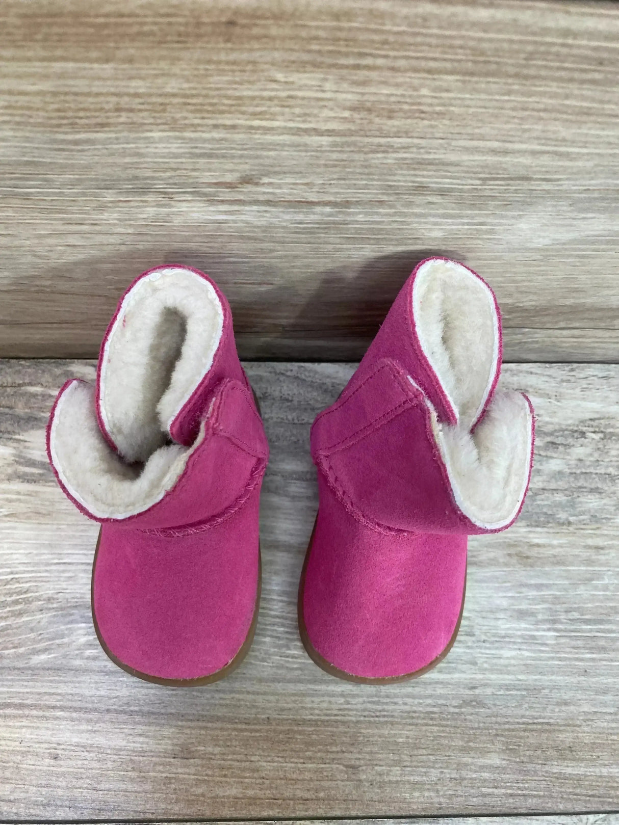 Top view of UGG Keelan toddler boots showcasing pink suede and folded cuffs with cream sheepskin lining on light wood