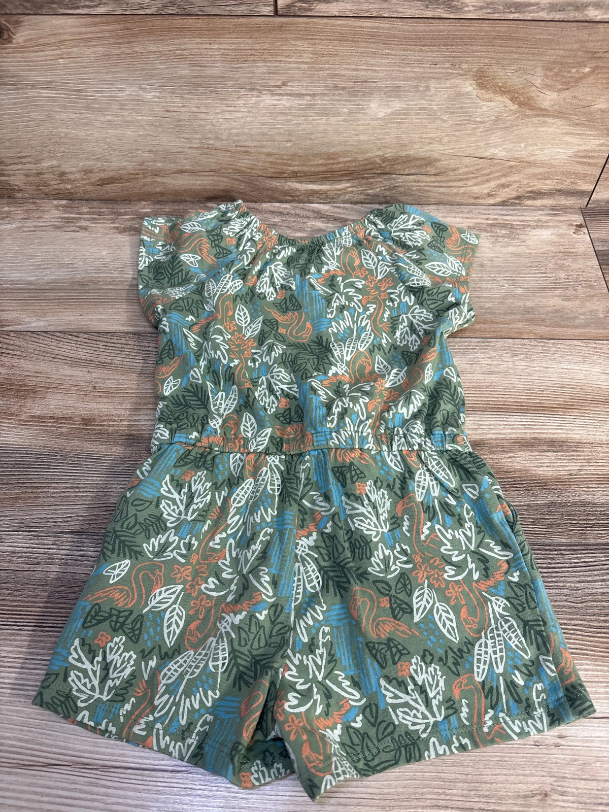 Top-down view of green Joe Fresh shortie romper with leafy print, fitted waist, and shorts-length legs on wood