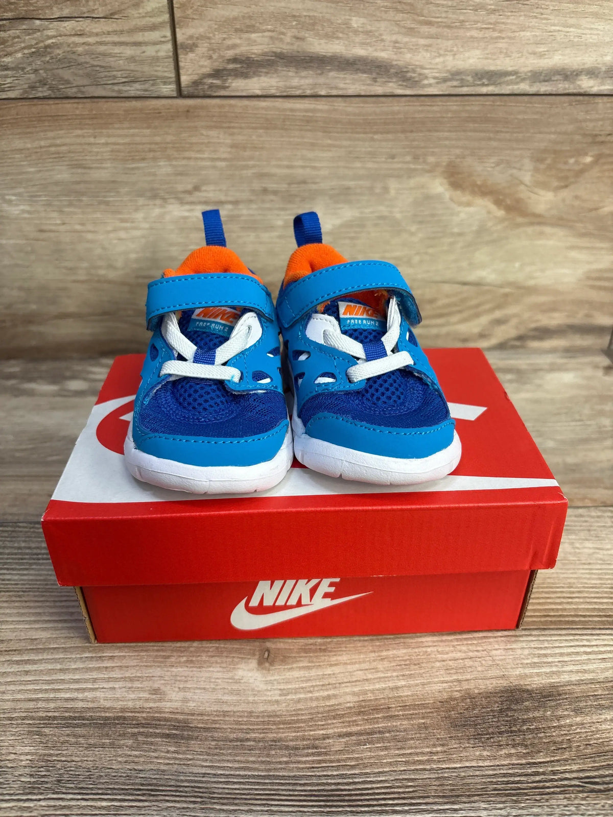 Front view of toddler Nike Free Run 2 sneakers in blue with orange lining, Velcro strap and white soles on red Nike box
