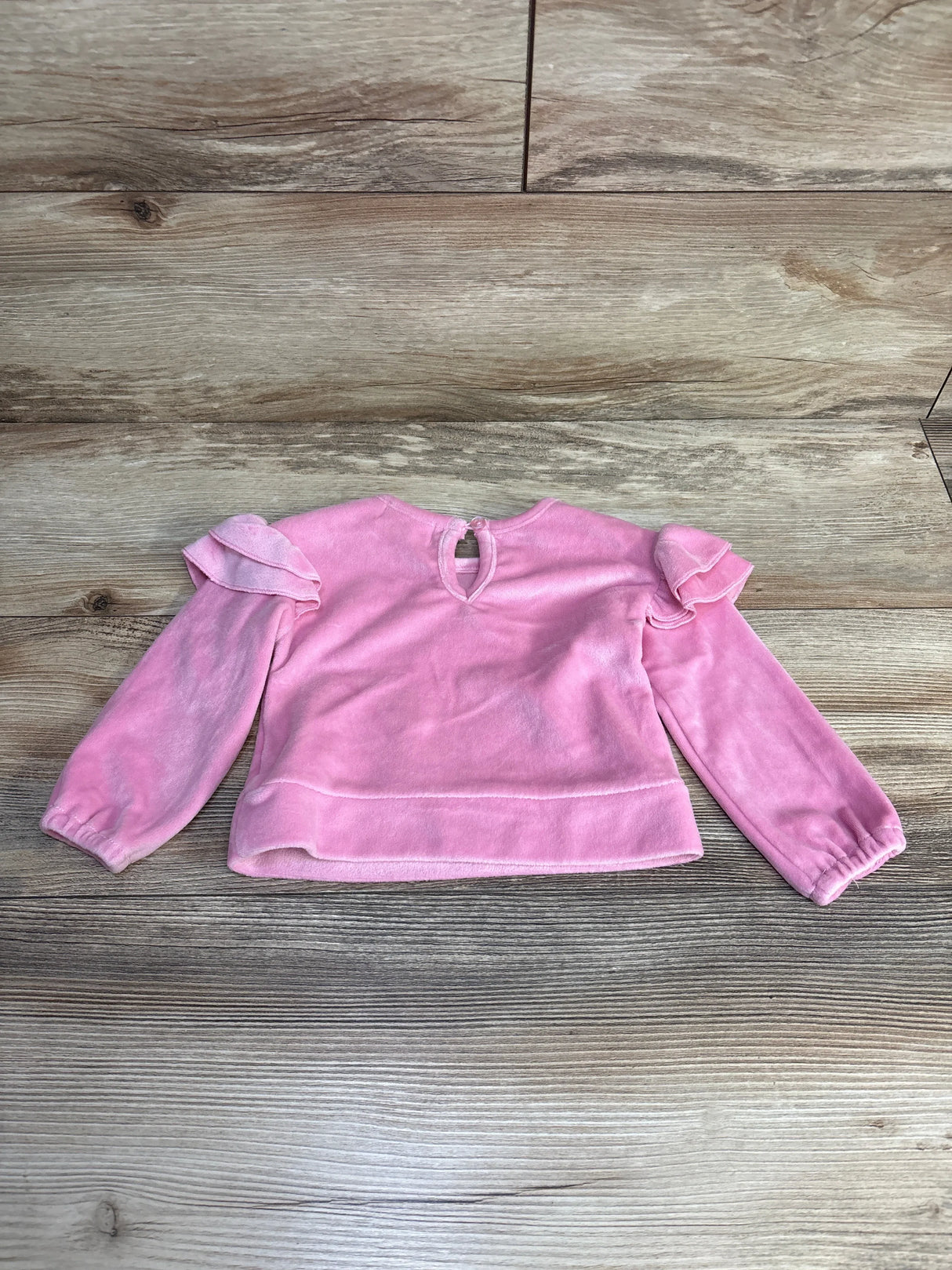Pink velvet toddler long sleeve top with ruffle shoulder details on wood background