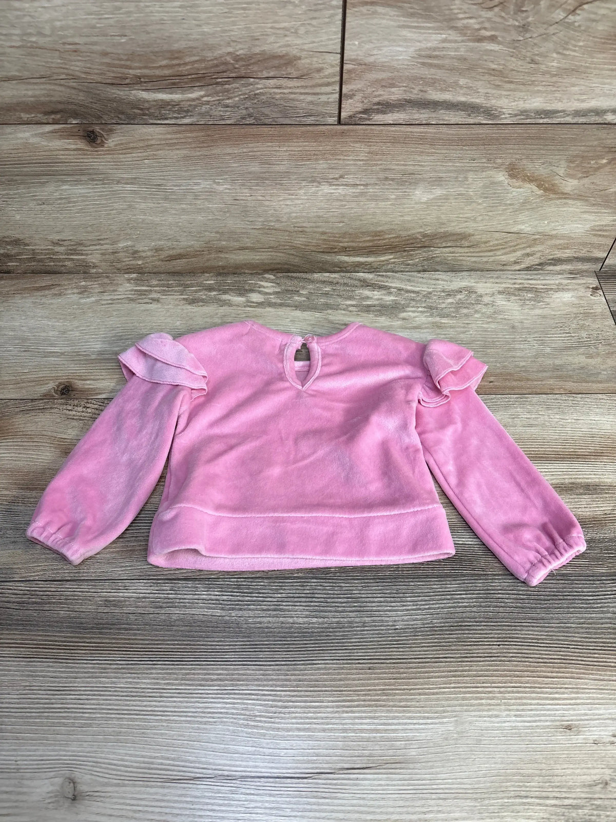 Pink velvet toddler long sleeve top with ruffle shoulder details on wood background