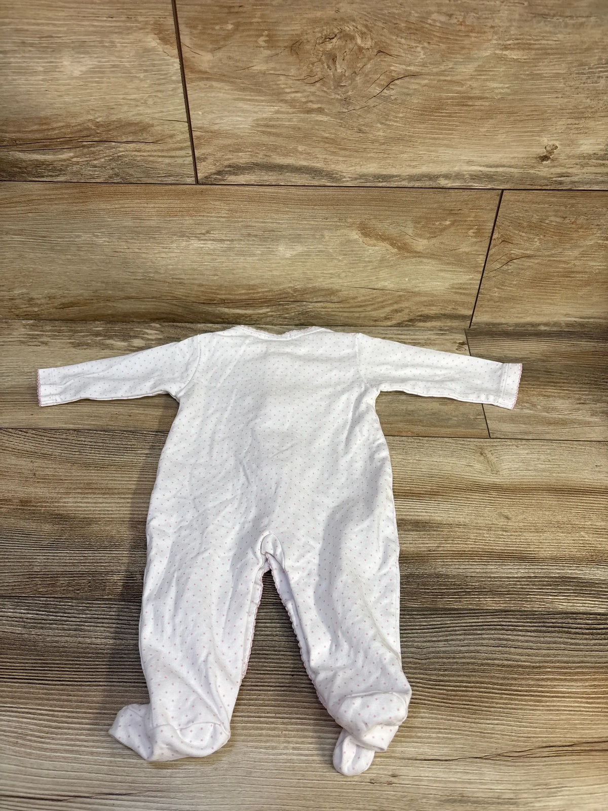 Full view of Kissy Kissy polka dot snap sleeper showcasing its white fabric, pink polka dots, and footed design on a wood floor