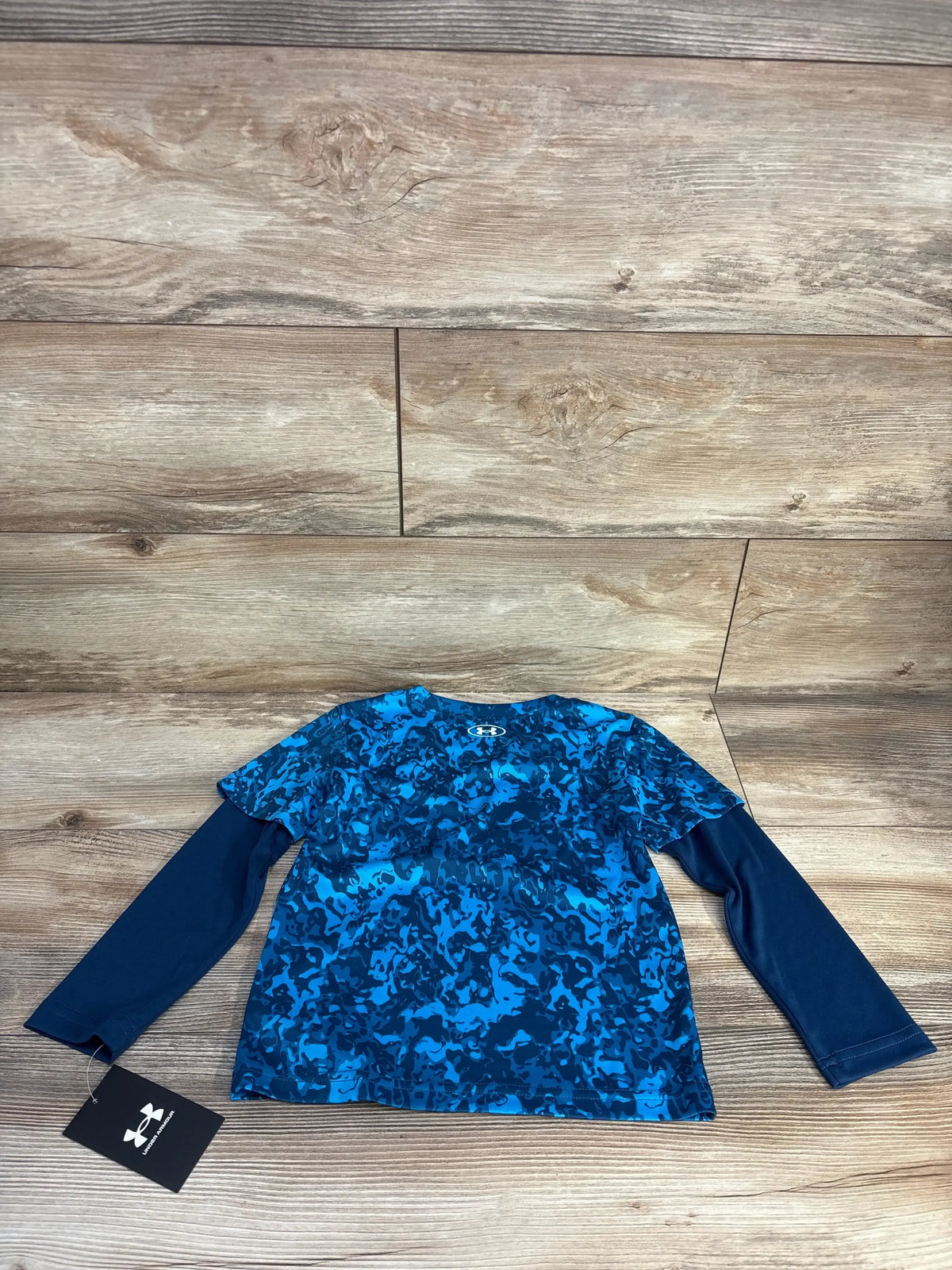 Flat lay of Under Armour mock layered long sleeve toddler shirt in blue camo, size 4T, showing layered look front and hang tag on wood background