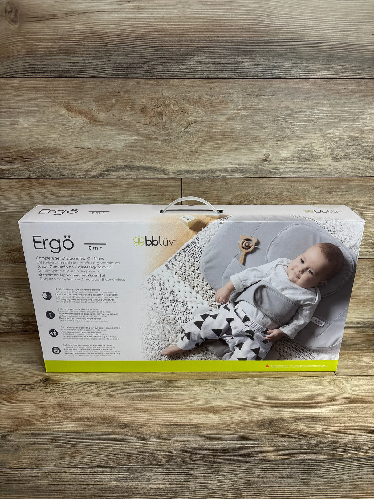 Front view of bbluv Ergo retail box showing gray ergonomic baby cushion with integrated harness and carrying handle on wood background