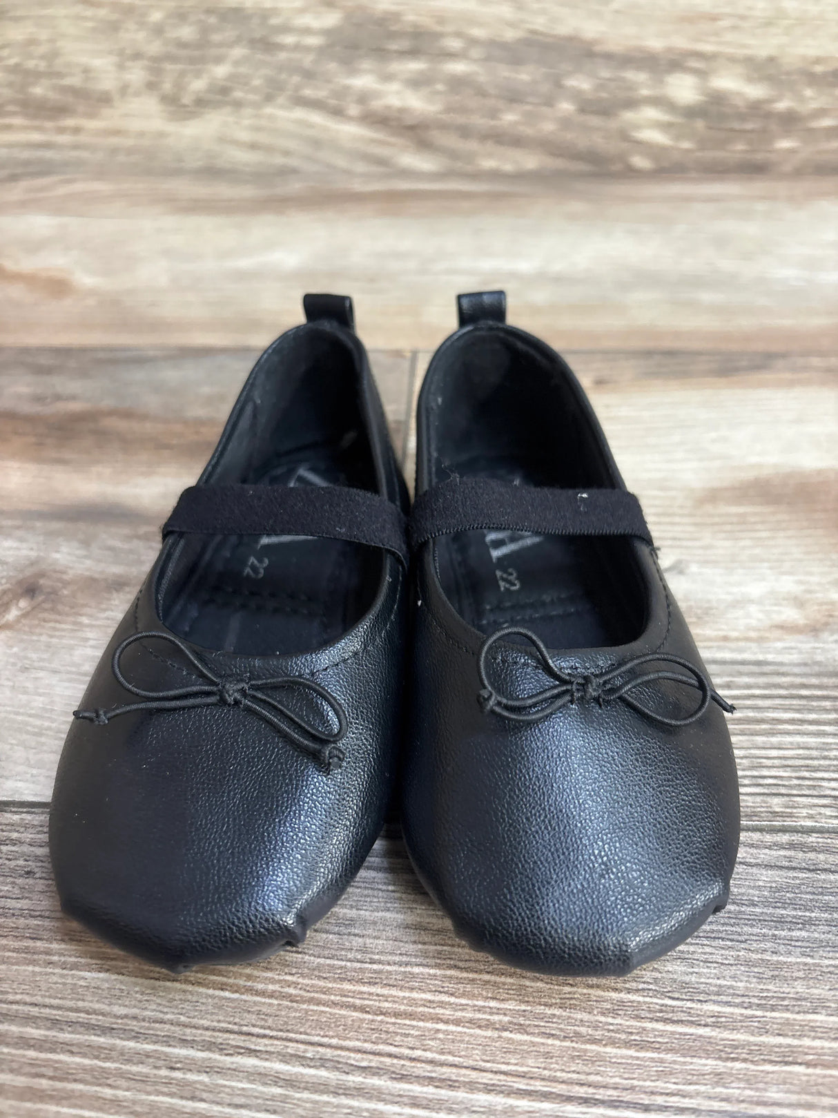 Front view of Zara Mary Jane flats in black, size 6C, showing elastic strap and bow accents on wood floor