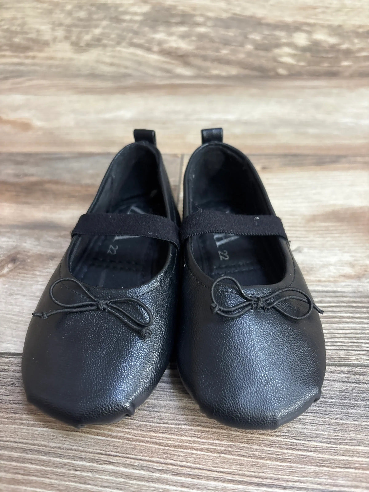 Front view of Zara Mary Jane flats in black, size 6C, showing elastic strap and bow accents on wood floor