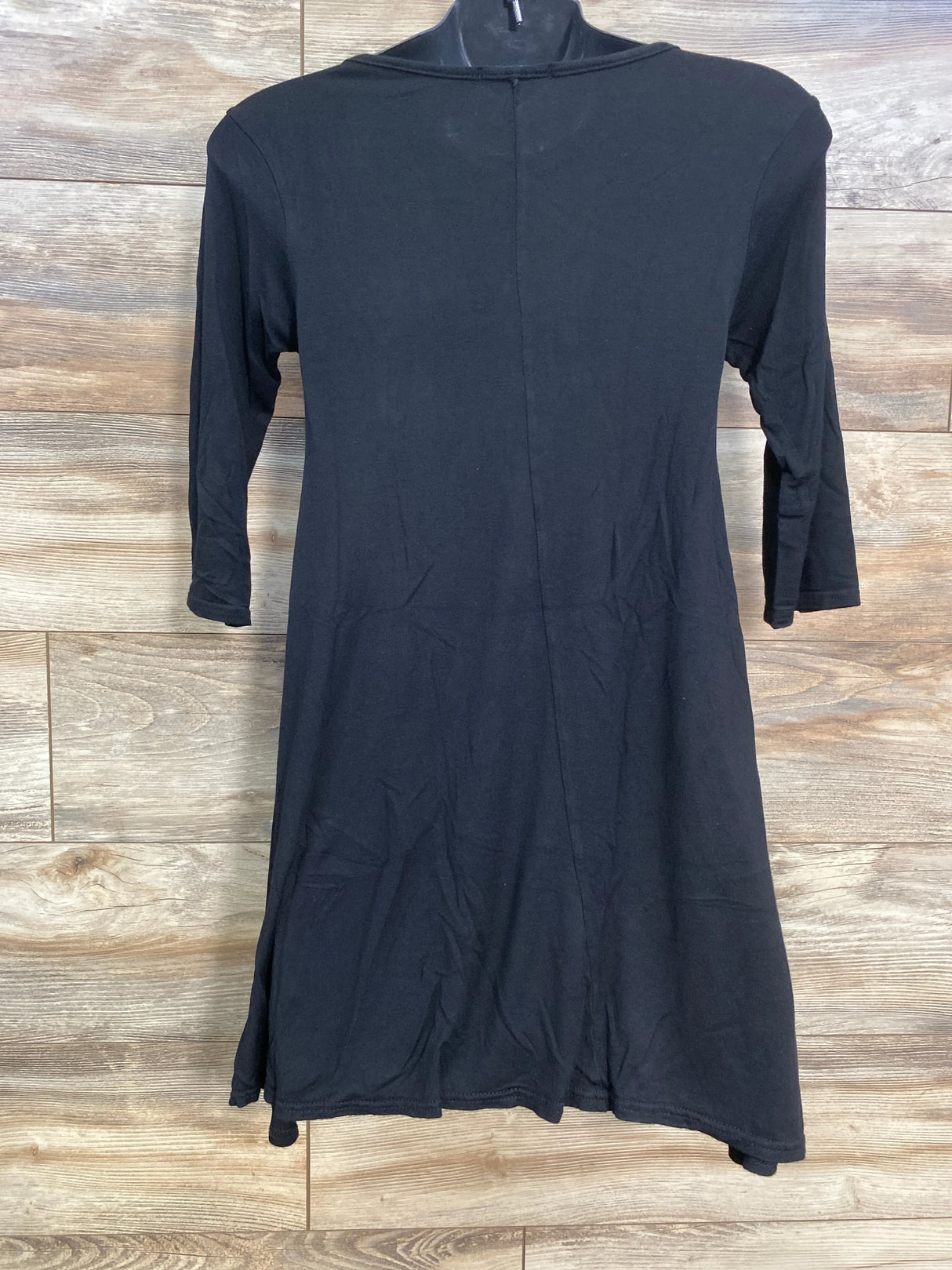 Back view of black maternity swing top showing 3/4 sleeves and flared swing hem on wood floor background