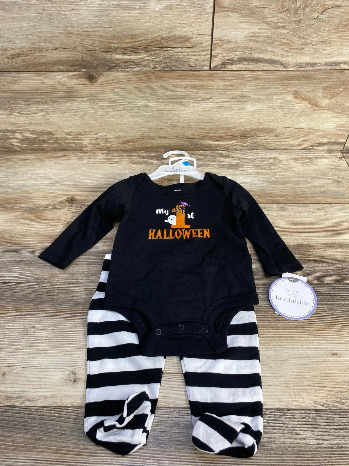 Front view of black Koala Baby bodysuit and pants set with My 1st Halloween graphic and striped pants on wood floor