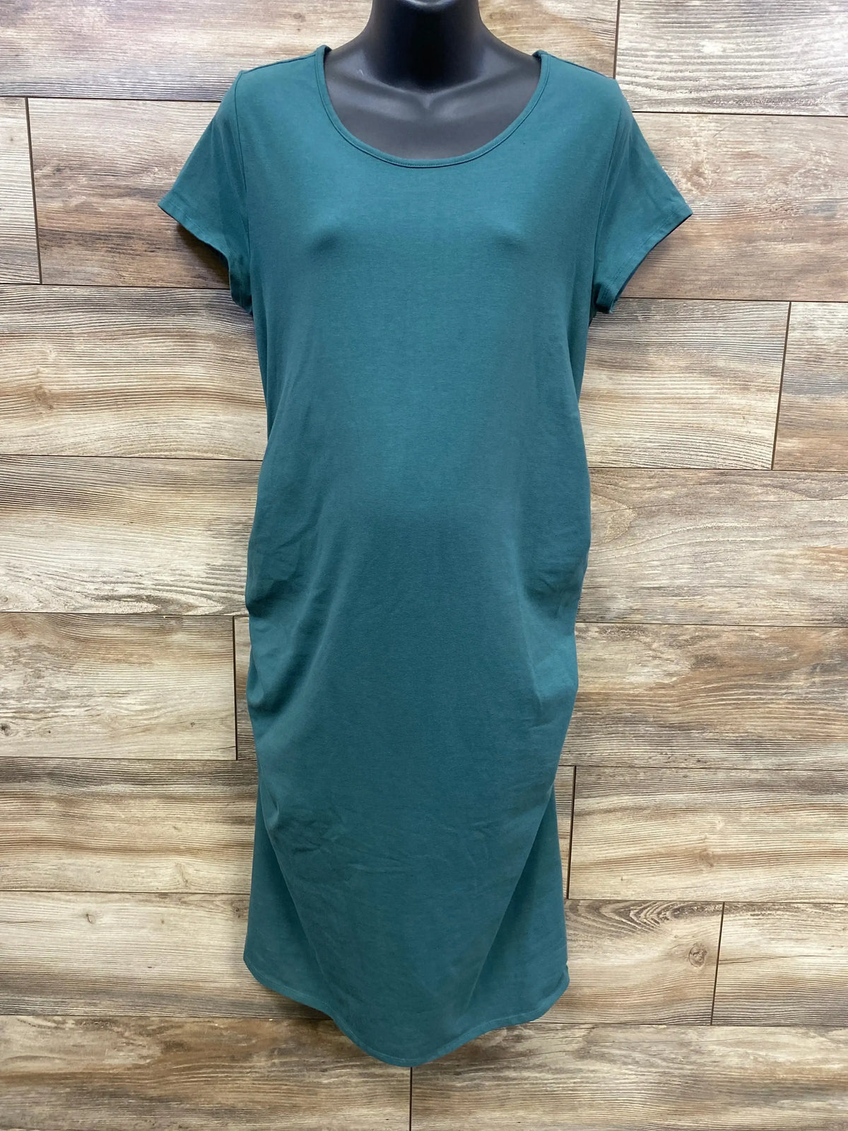 Front of green maternity bodycon dress (XL) with scoop neck, short sleeves, fitted silhouette on black mannequin against wood background